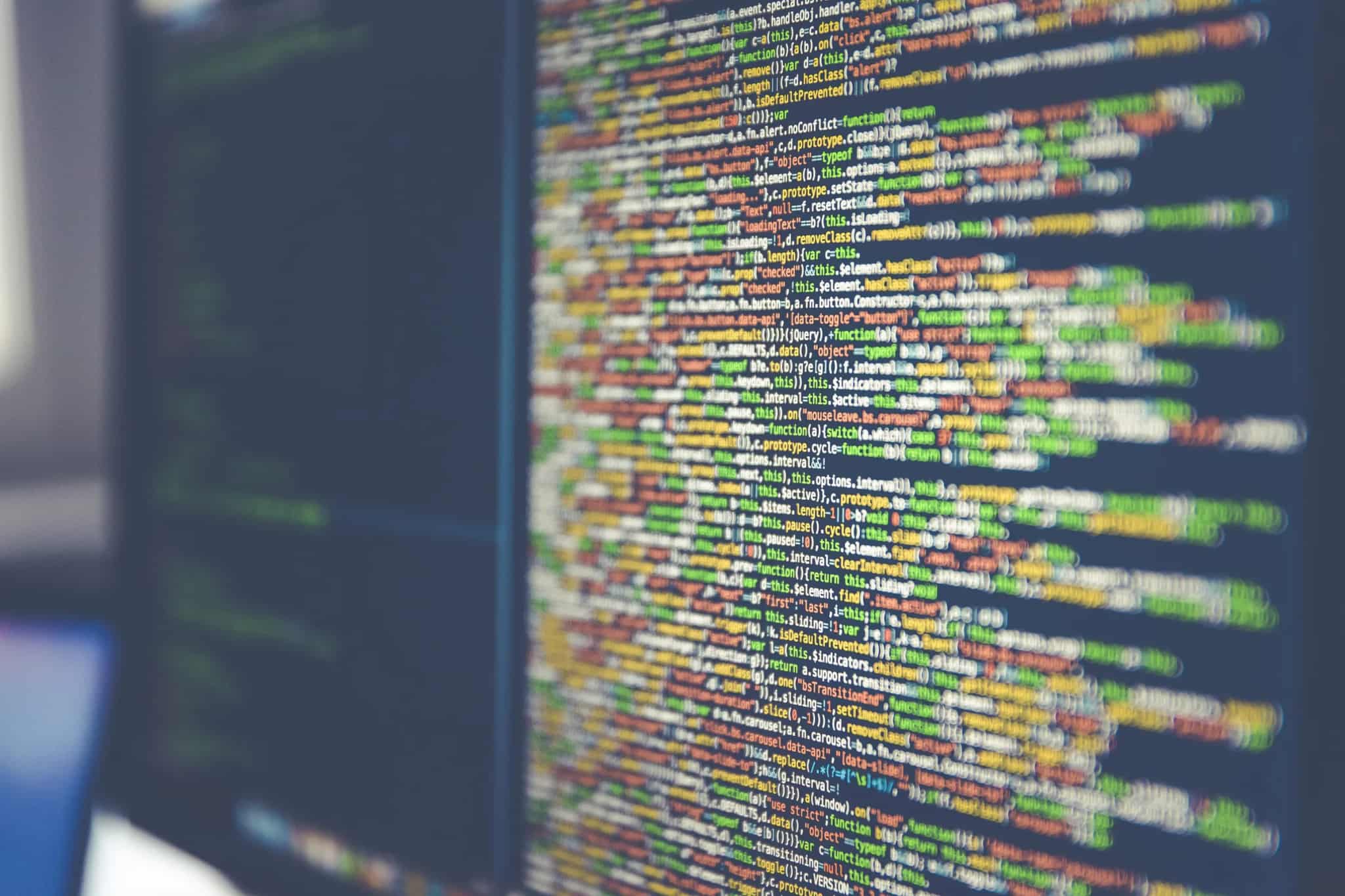 Extreme close-up of colorful lines of computer code glowing on a dark monitor screen.