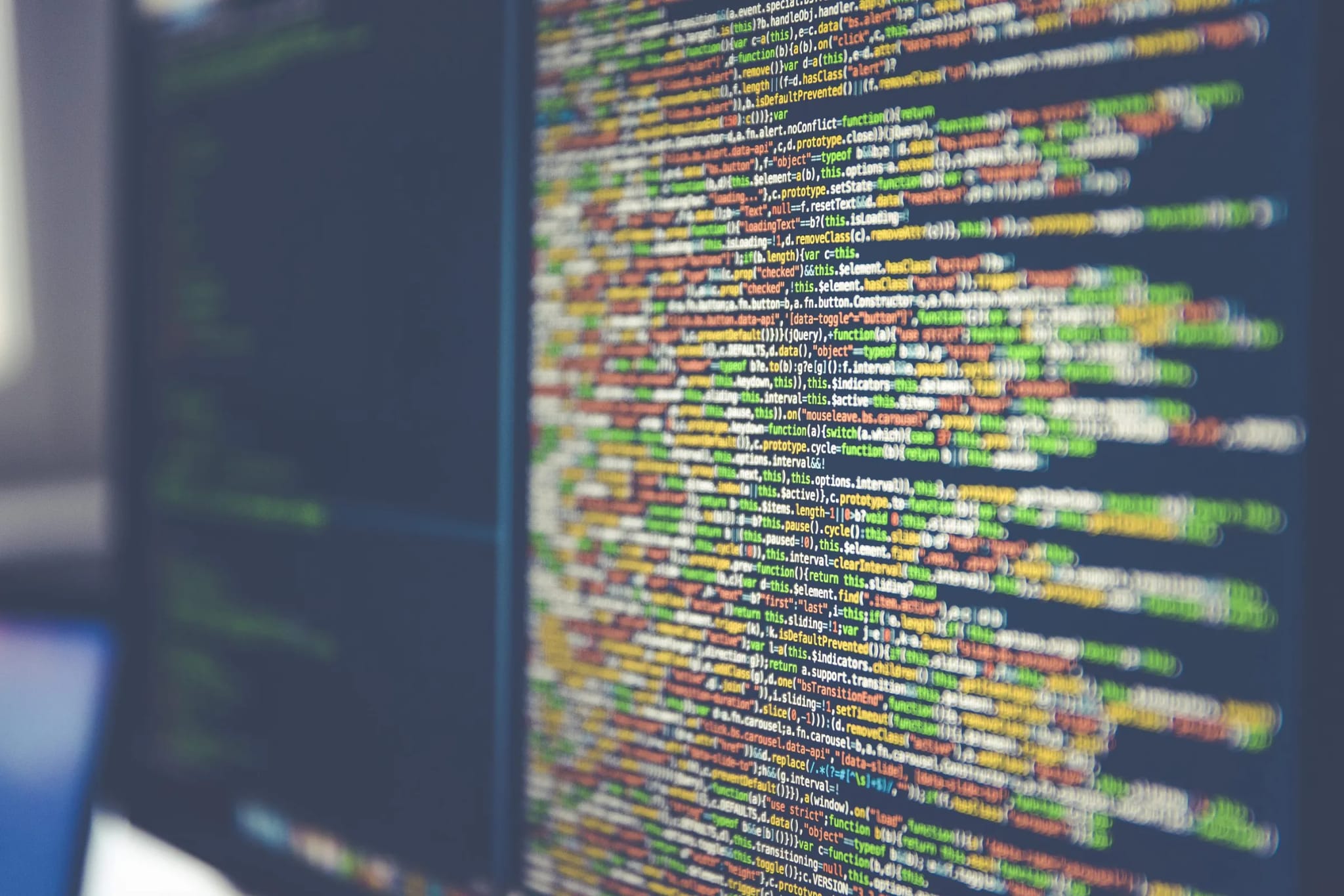 Extreme close-up of colorful lines of computer code glowing on a dark monitor screen.