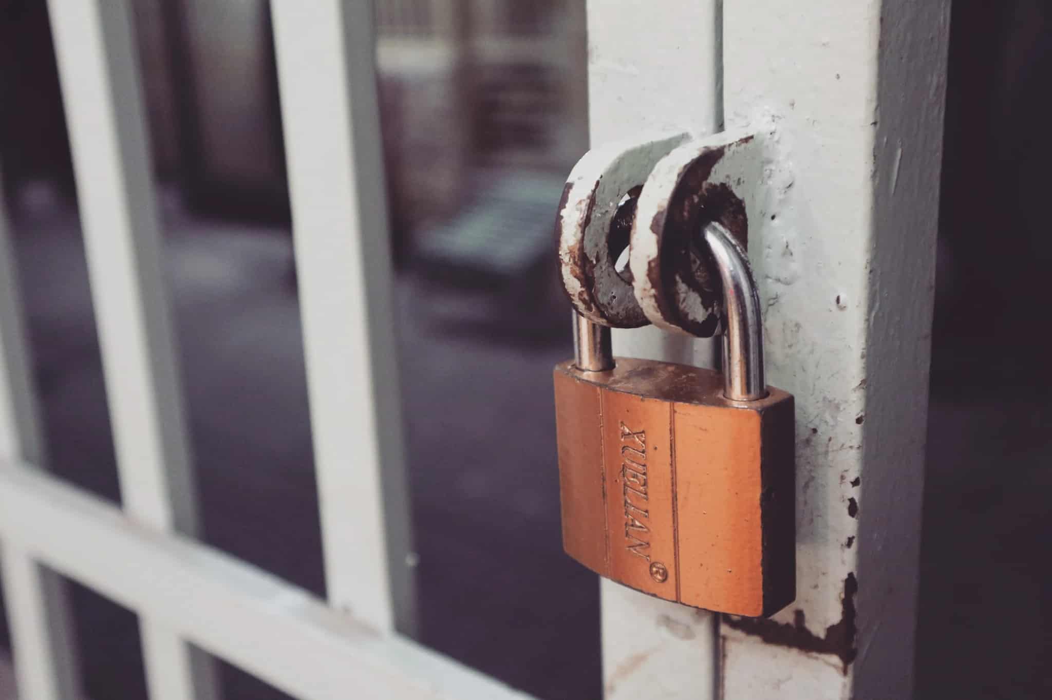 Close-up photo of a brass padlock securing a weathered white metal gate.