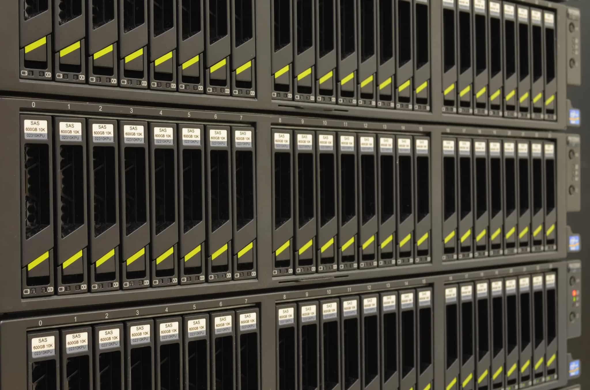 Close-up of rows of hard-drive bays with yellow release tabs inside a server rack.