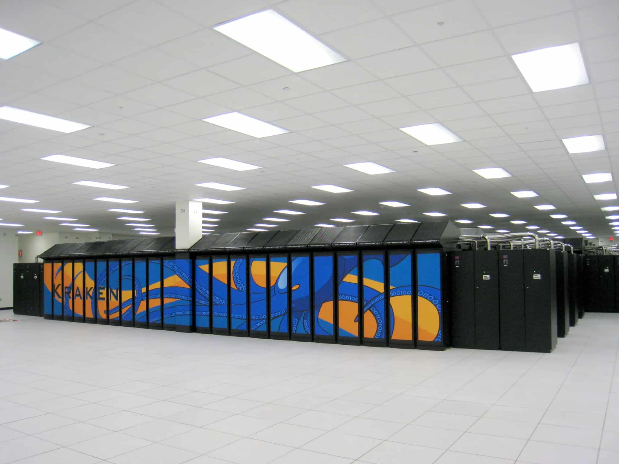 A long row of tall black server cabinets stretching down an aisle of a large data center under fluorescent lighting.