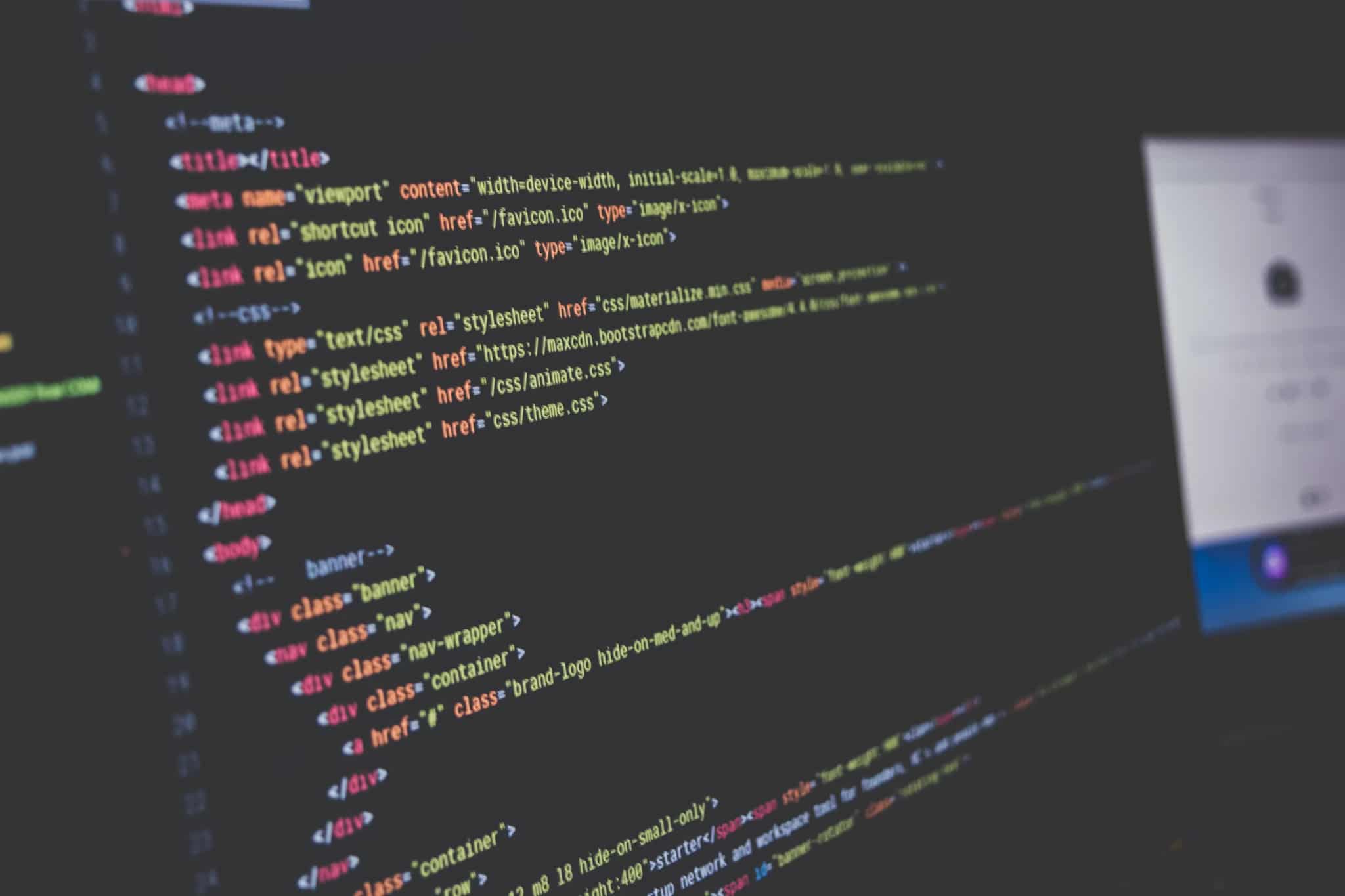 Close-up of a computer monitor displaying lines of colorful code in a dimly lit room.