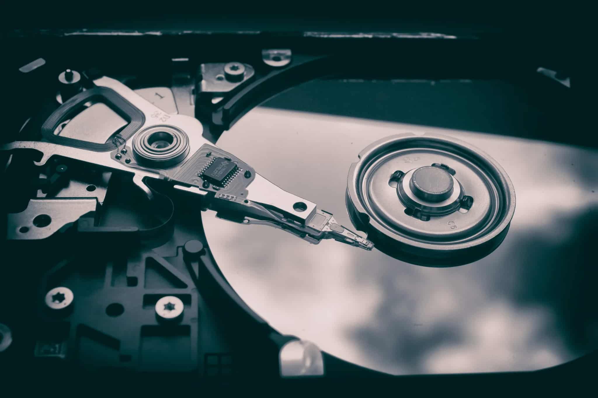 A black-and-white macro shot of the internal read/write head and spinning platter of an open hard disk drive.