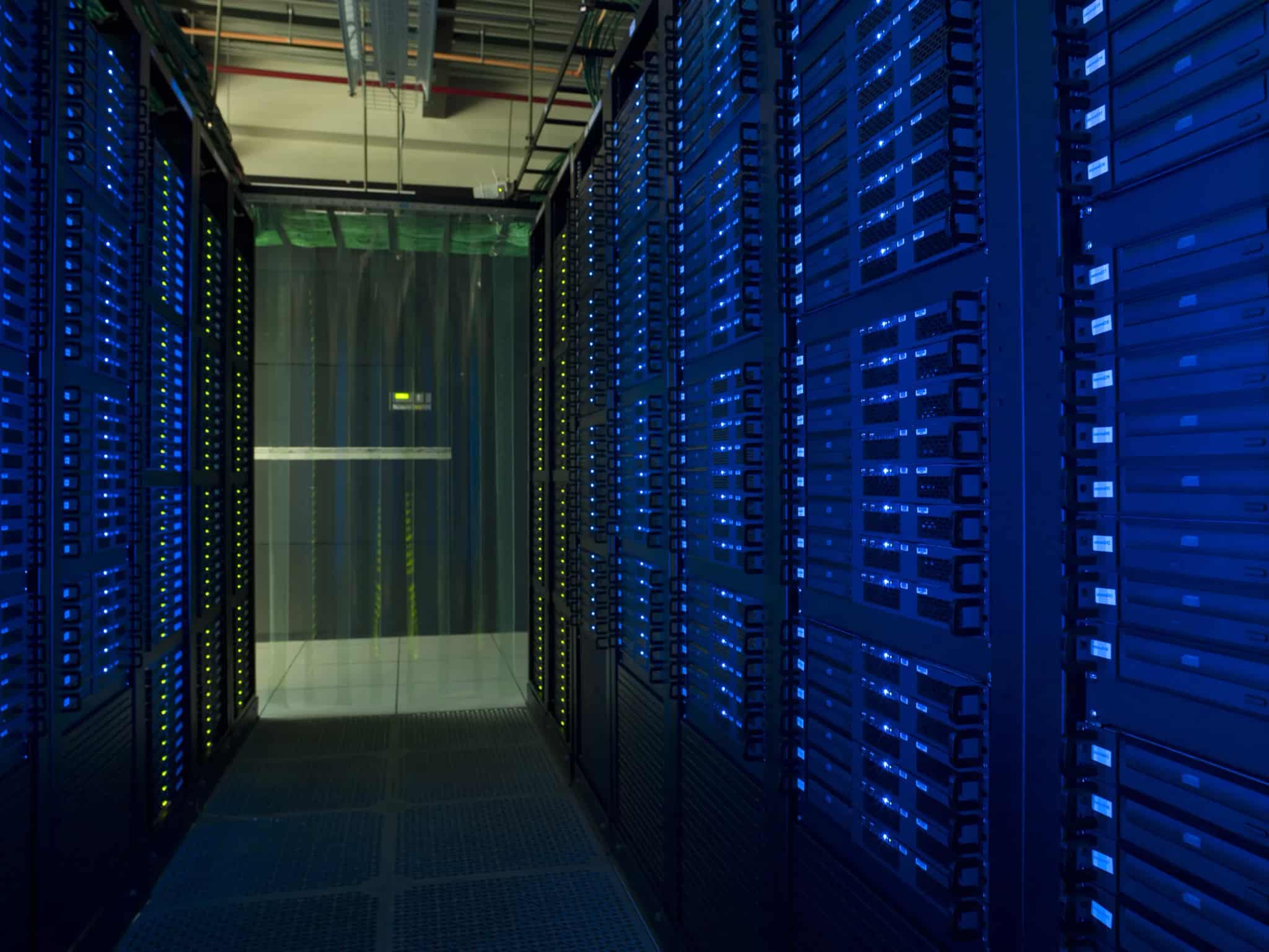 A long row of server racks glowing with blue and green status lights in a dimly lit data center corridor.