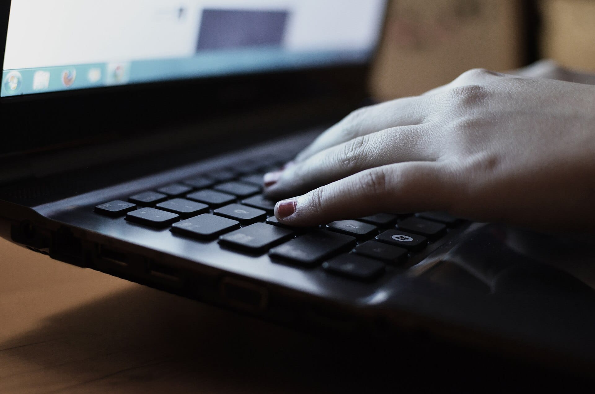 Close-up of a hand typing on a laptop keyboard with a blurred screen glowing in the background.