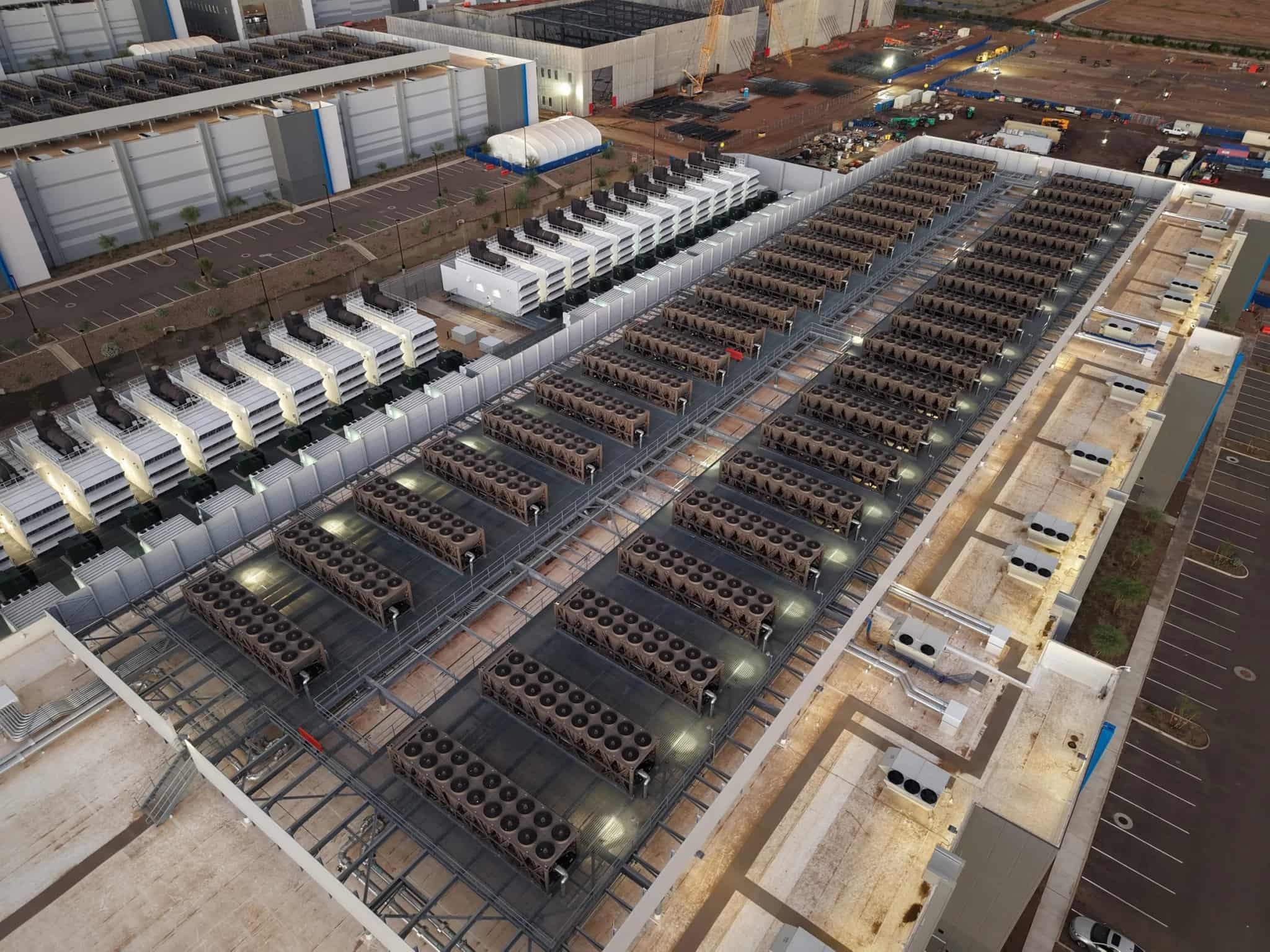 Aerial view of a large data center campus with long rows of rooftop cooling units at dusk.