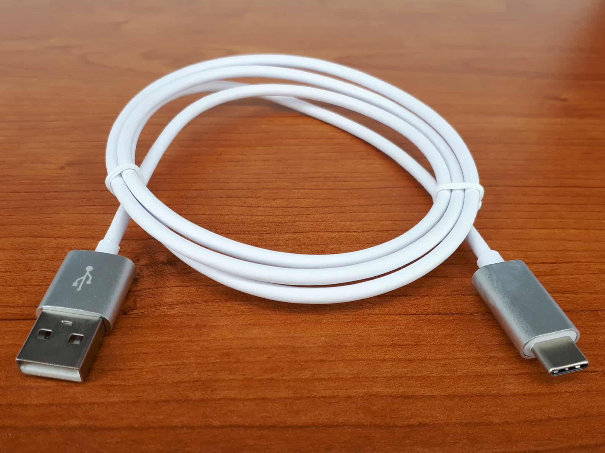 A white USB cable with metal connectors coiled neatly on a wooden table.