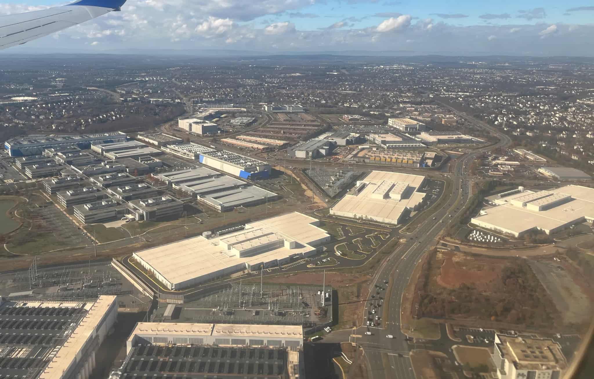 An aerial view from an airplane window of a large data center campus surrounded by suburban neighborhoods.