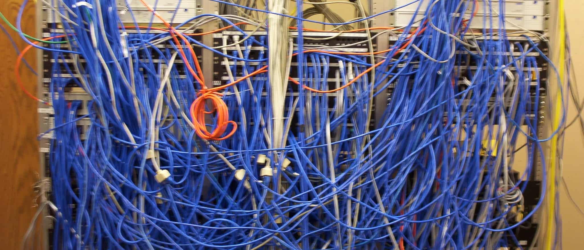 A server rack overwhelmed by a dense tangle of blue and gray network cables.