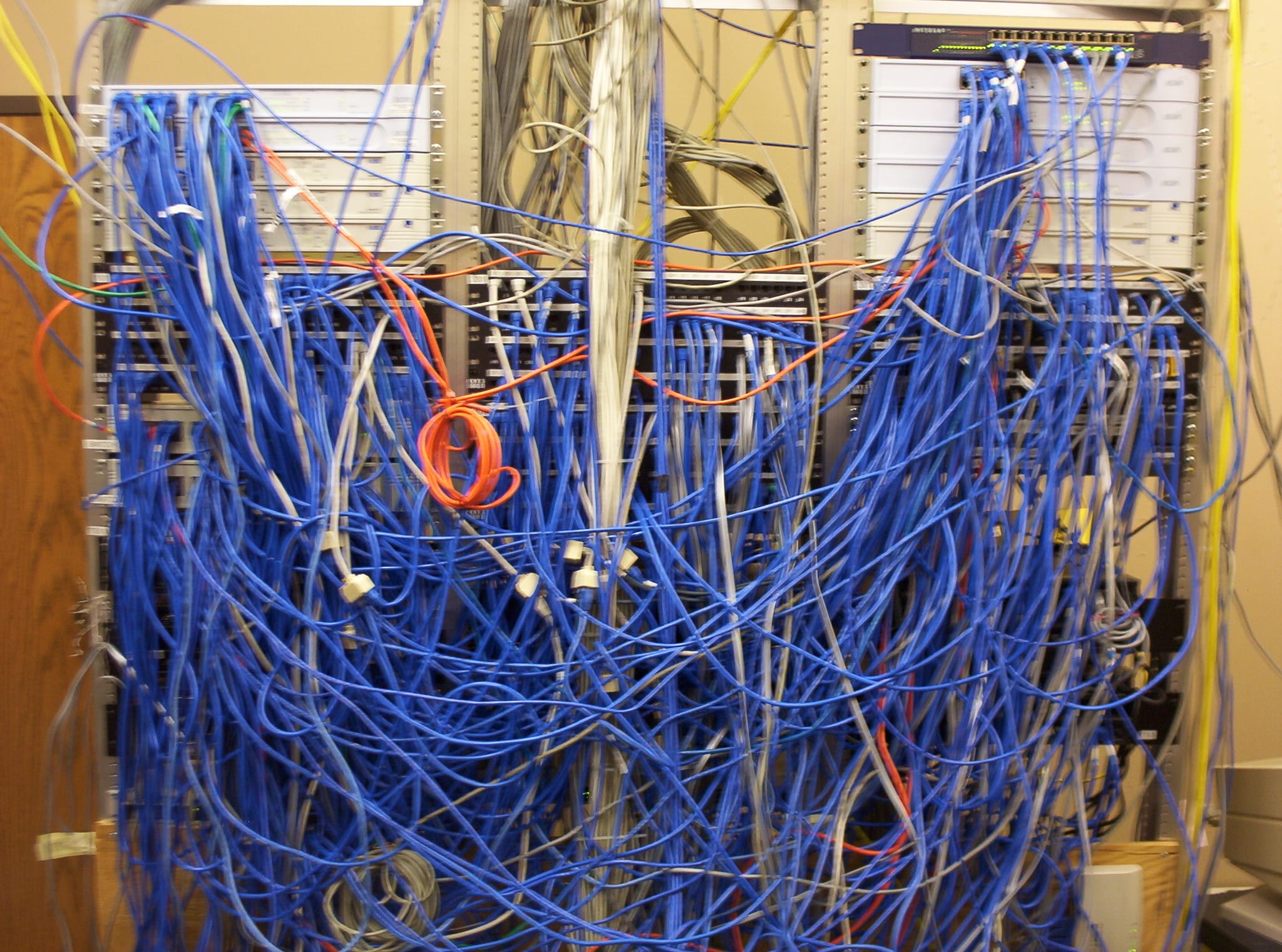 A server rack overwhelmed by a dense tangle of blue and gray network cables.