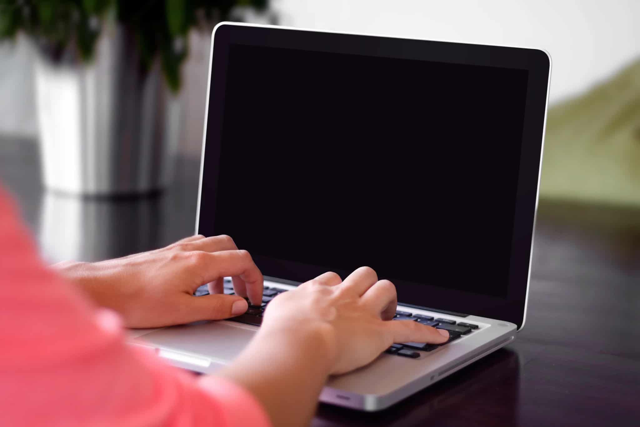 A person's hands typing on a laptop keyboard with a blurred green background.
