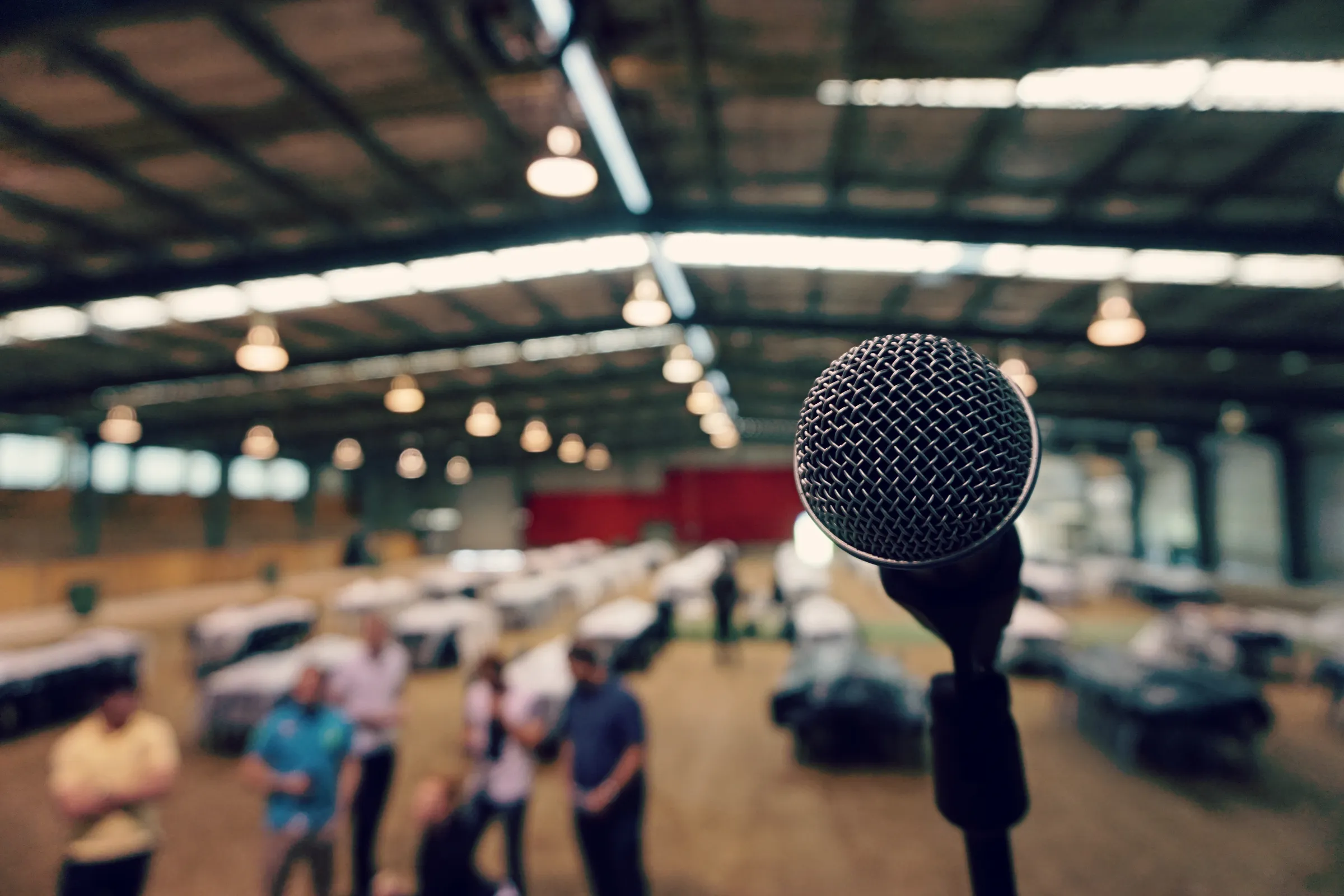 Close-up of a microphone on a stand with blurred people in a large hall behind it.