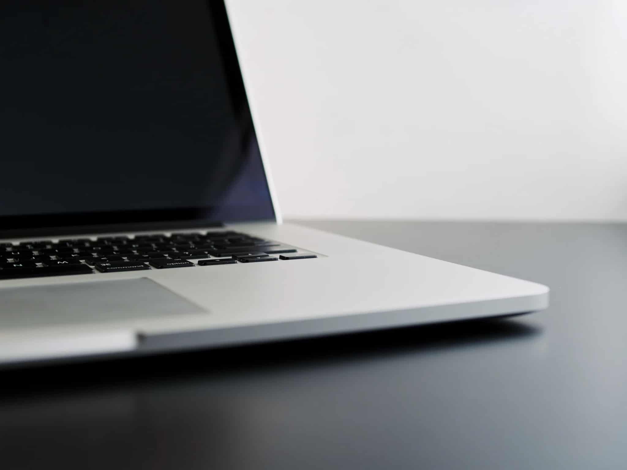 Close-up side view of an open laptop with its dimmed screen, sitting on a dark desk.