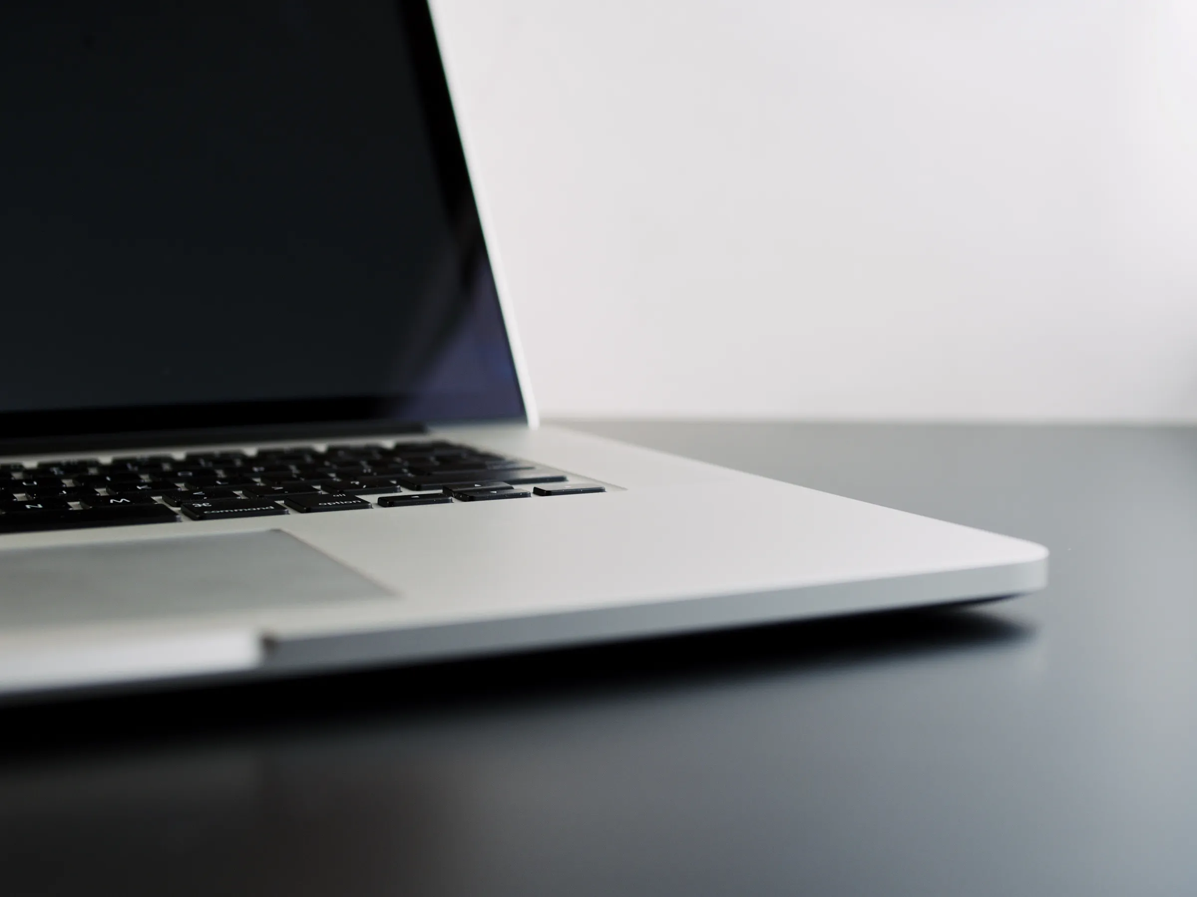 Close-up side view of an open laptop with its dimmed screen, sitting on a dark desk.