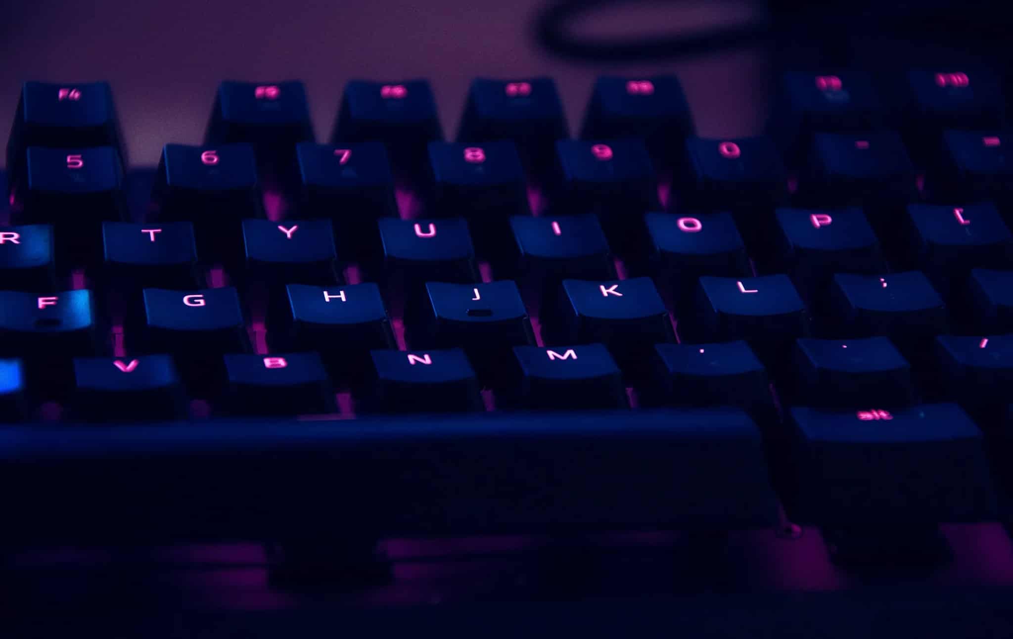Close-up of a dark mechanical keyboard with pink backlit keys.
