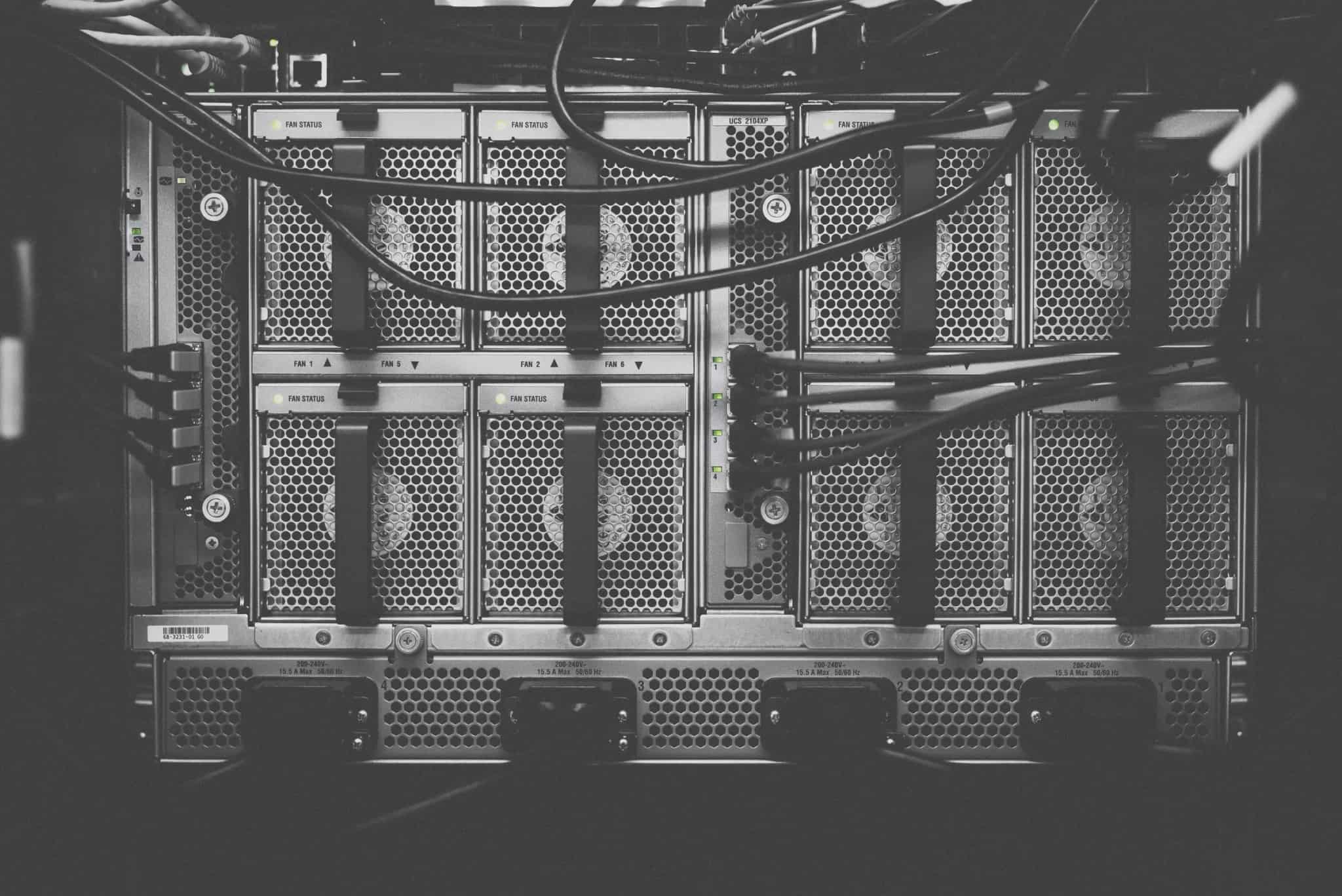 A black-and-white close-up of a server's rear panel with cooling fans and tangled network cables.