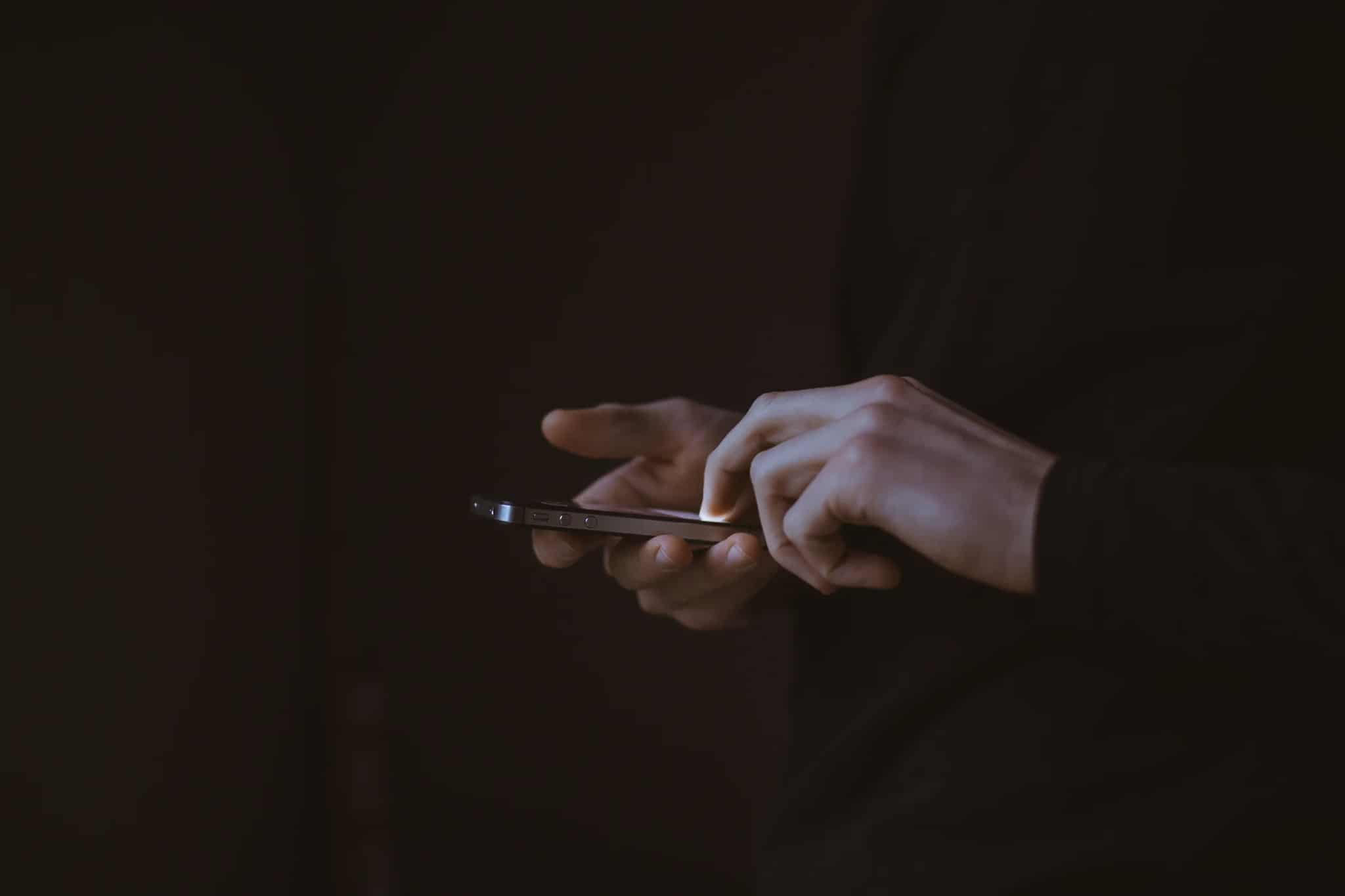 A person's hands holding and touching a smartphone in low light.