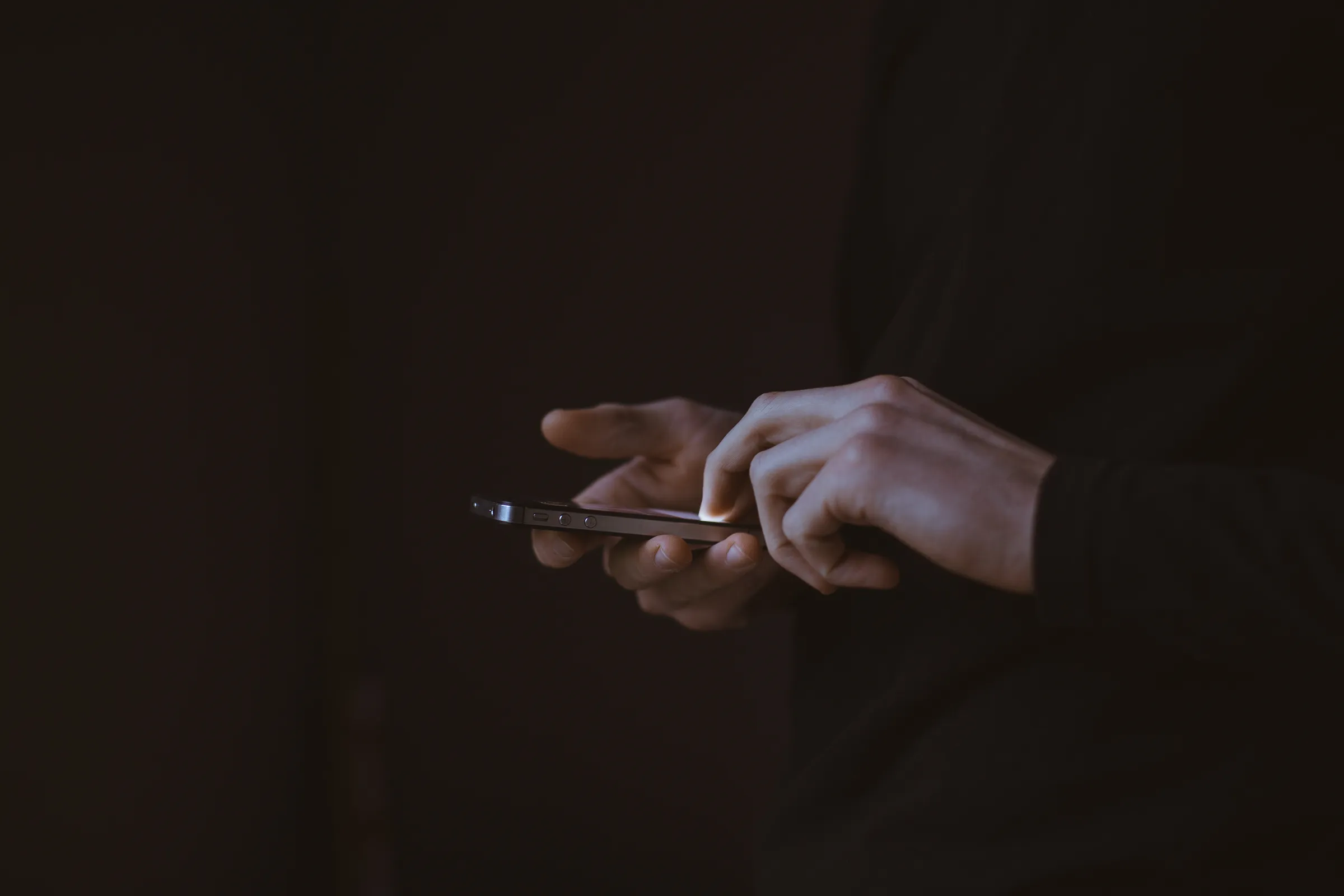 A person's hands holding and touching a smartphone in low light.