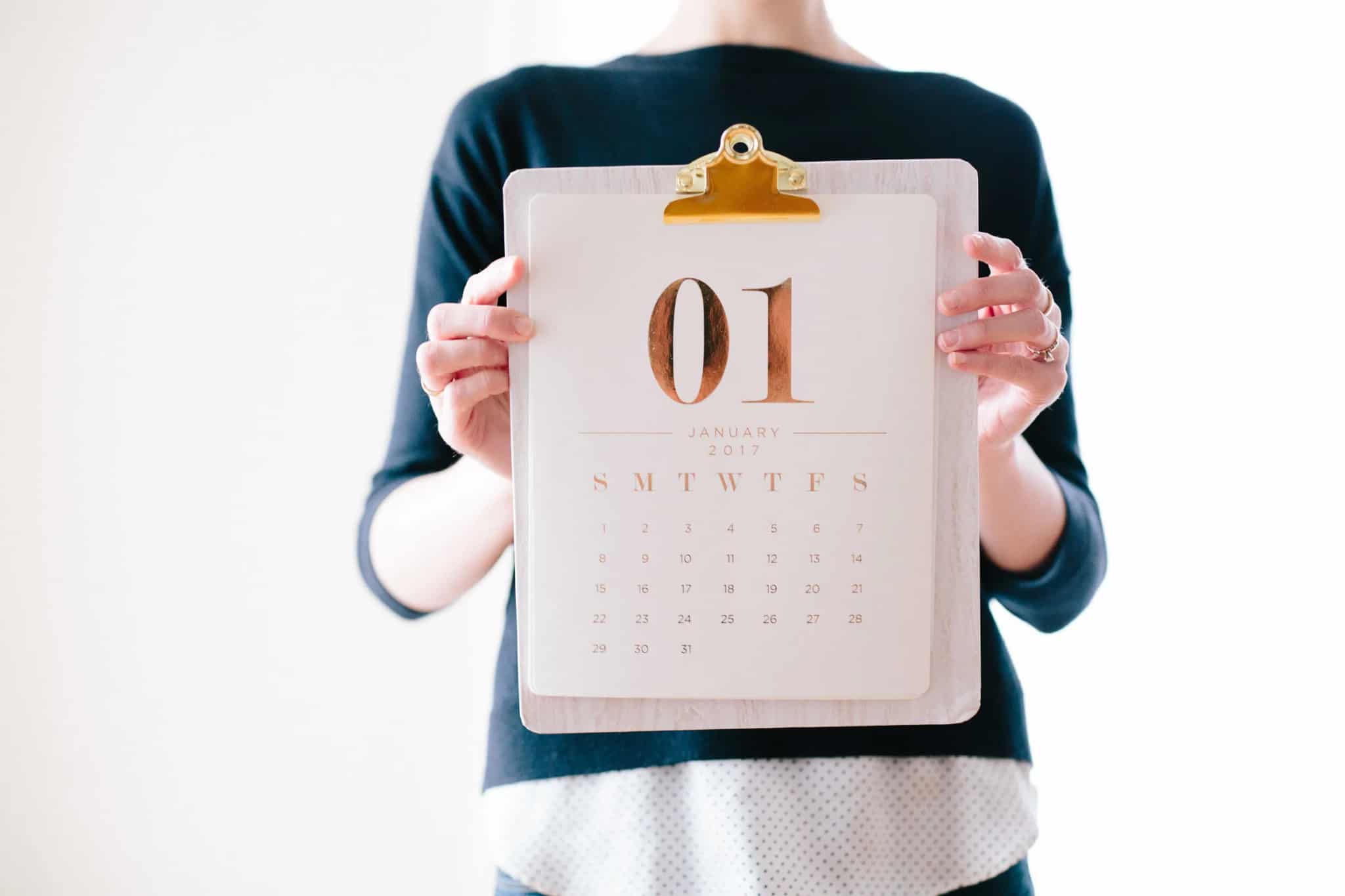 A person holding up a clipboard with a paper wall calendar showing the month of January.
