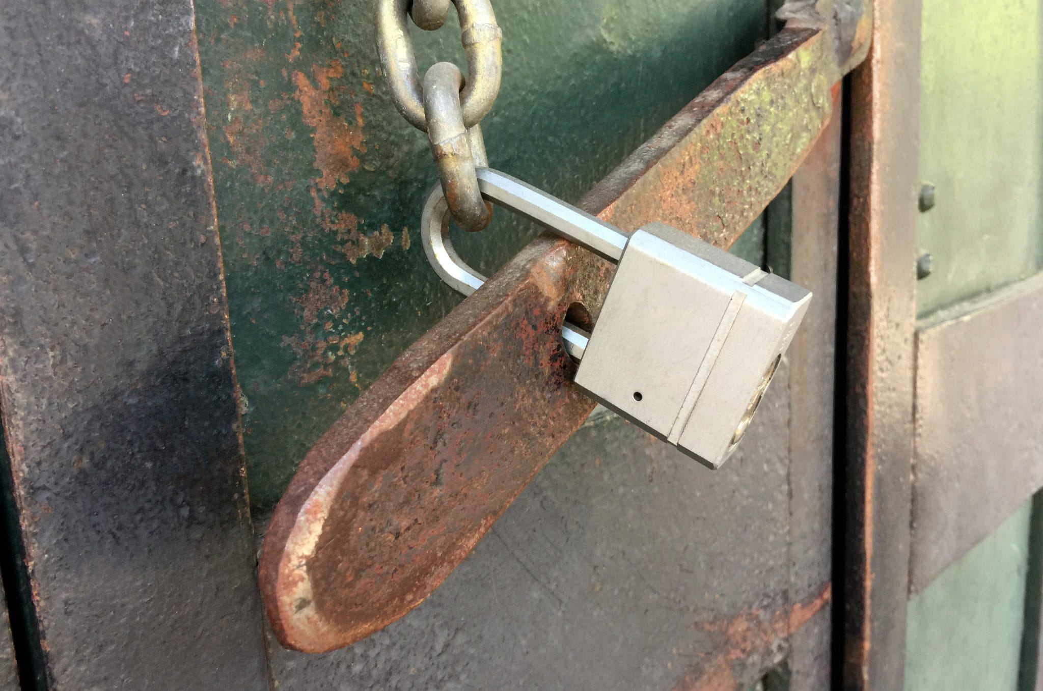 A rusty padlock securing a chain on an old, weathered metal door.