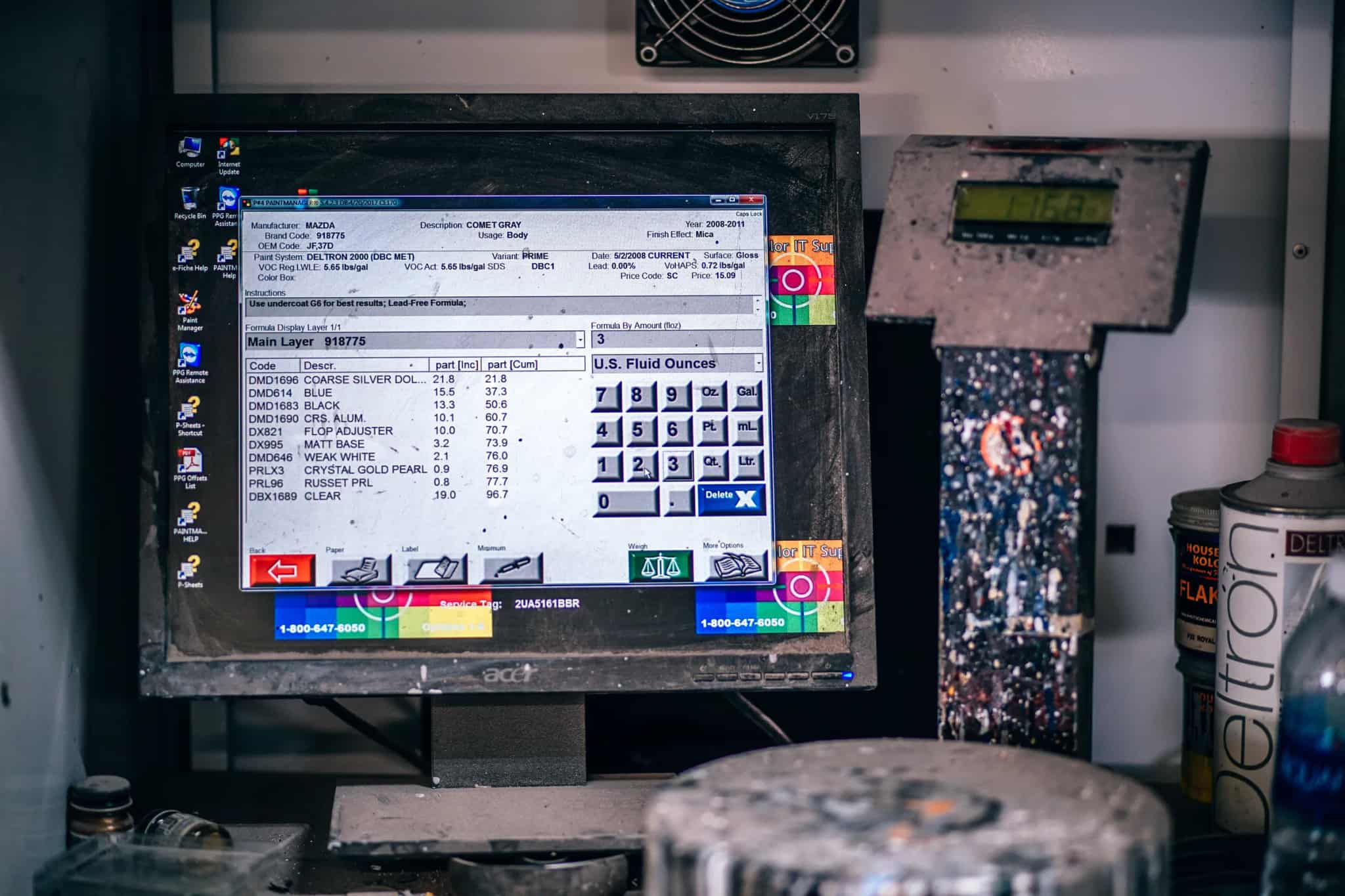 A dusty, well-worn computer monitor running old paint-formula software in a cluttered workshop, surrounded by paint cans and equipment.