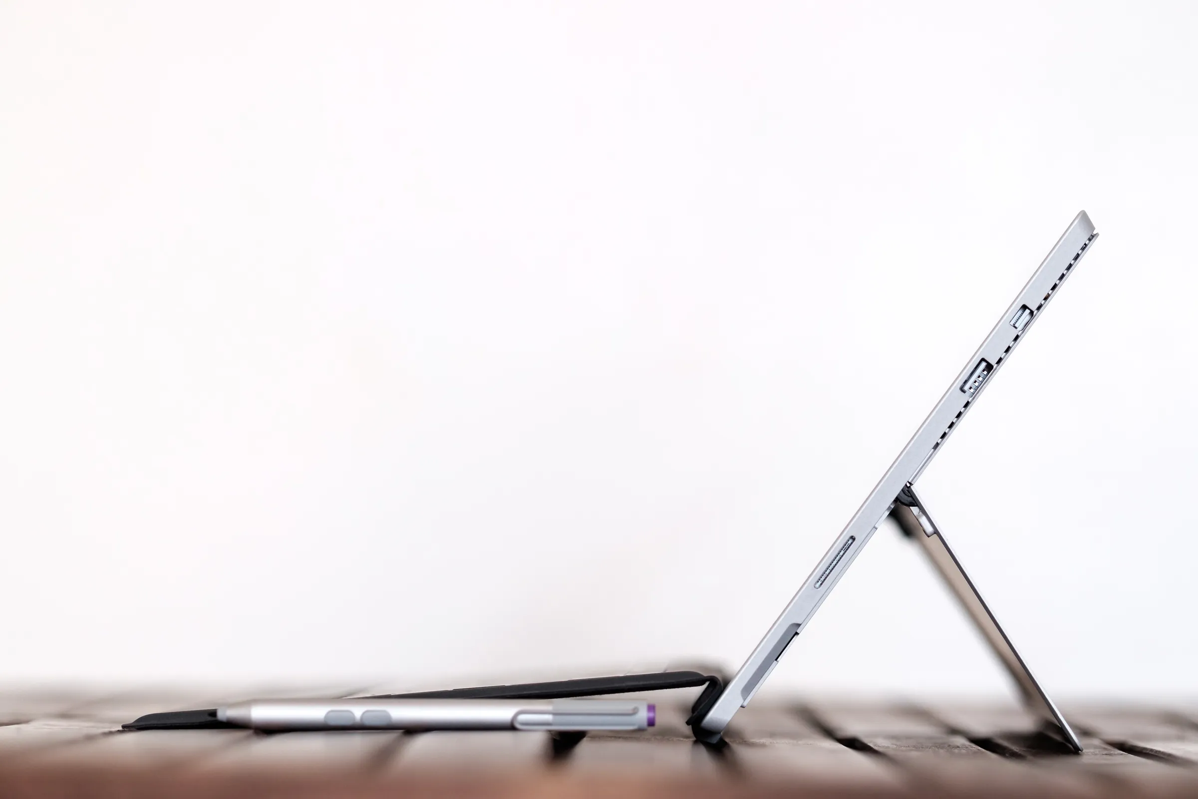 Side profile of a tablet computer propped up on its kickstand next to a stylus pen.