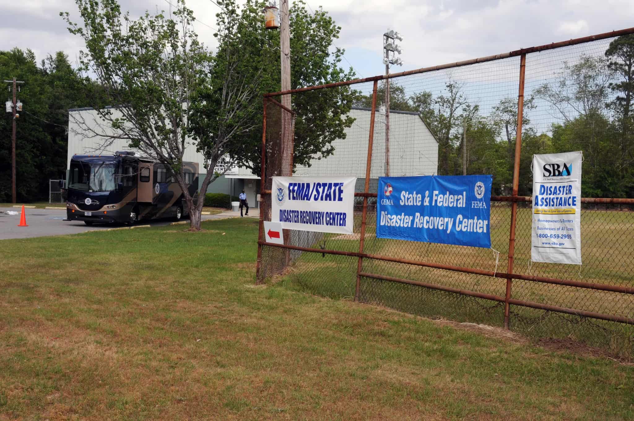 A mobile disaster recovery vehicle parked outside a community building, with recovery center signage on a fence nearby.