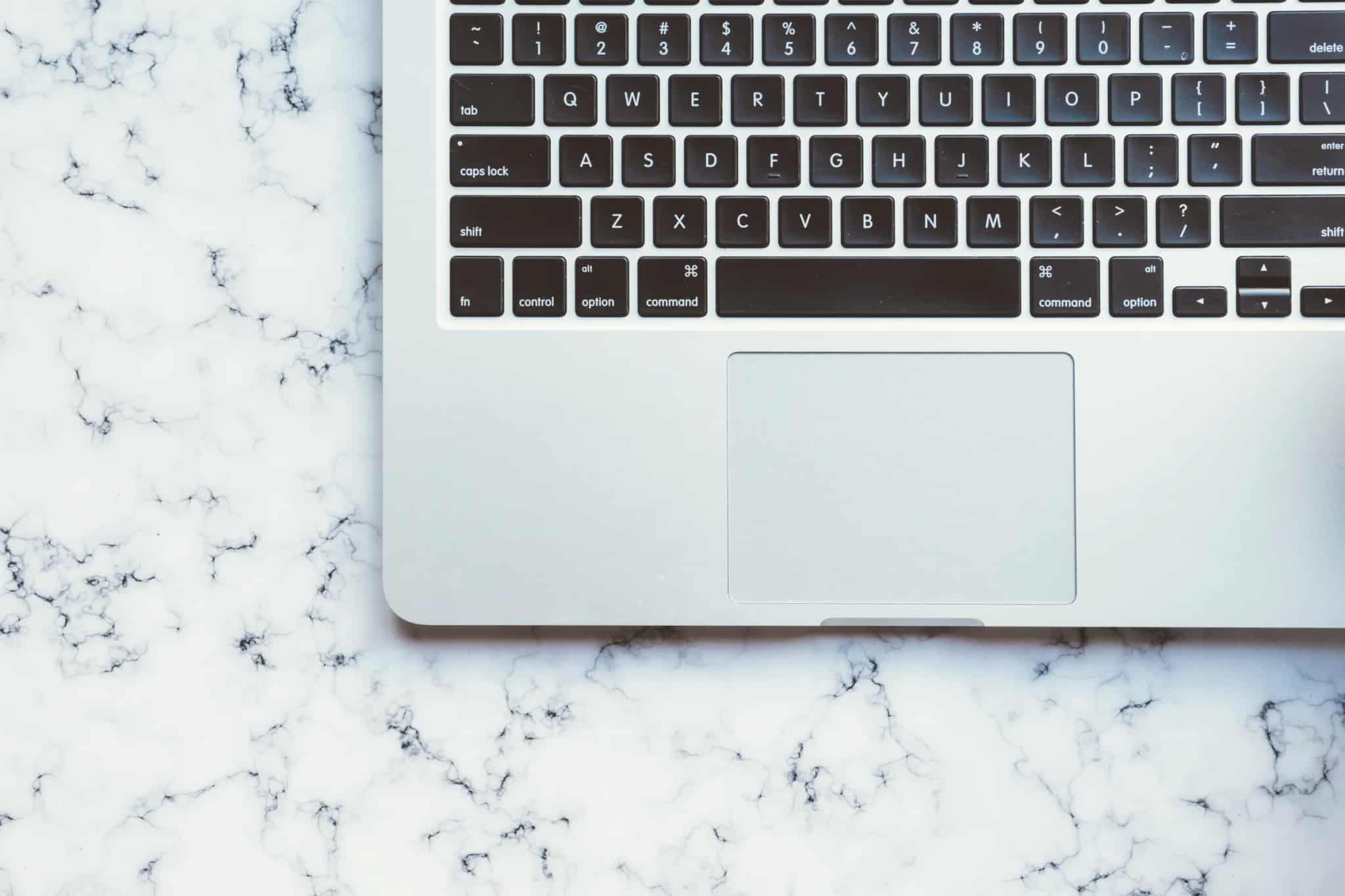 Overhead view of a laptop keyboard and trackpad resting on a white marble surface.