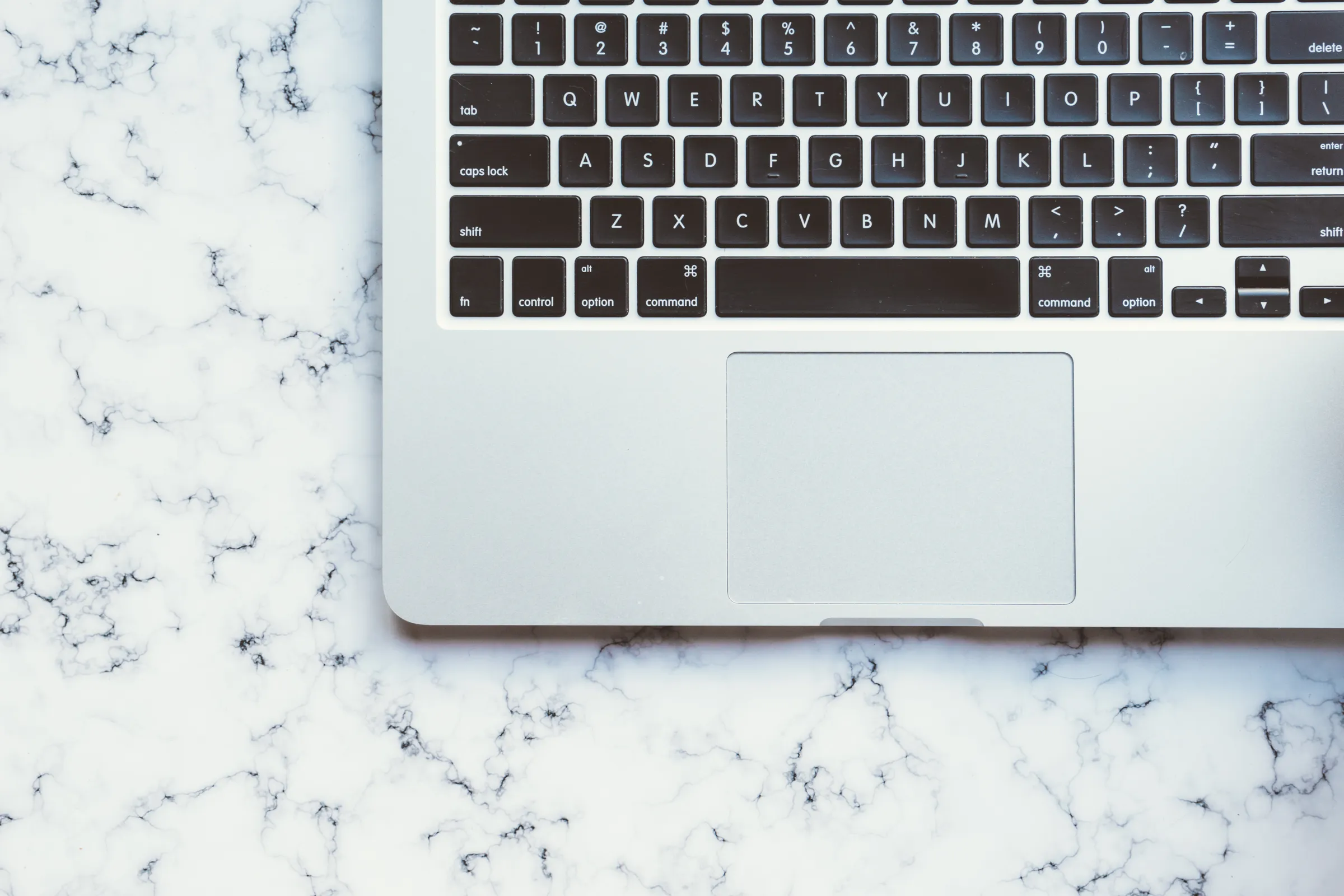 Overhead view of a laptop keyboard and trackpad resting on a white marble surface.