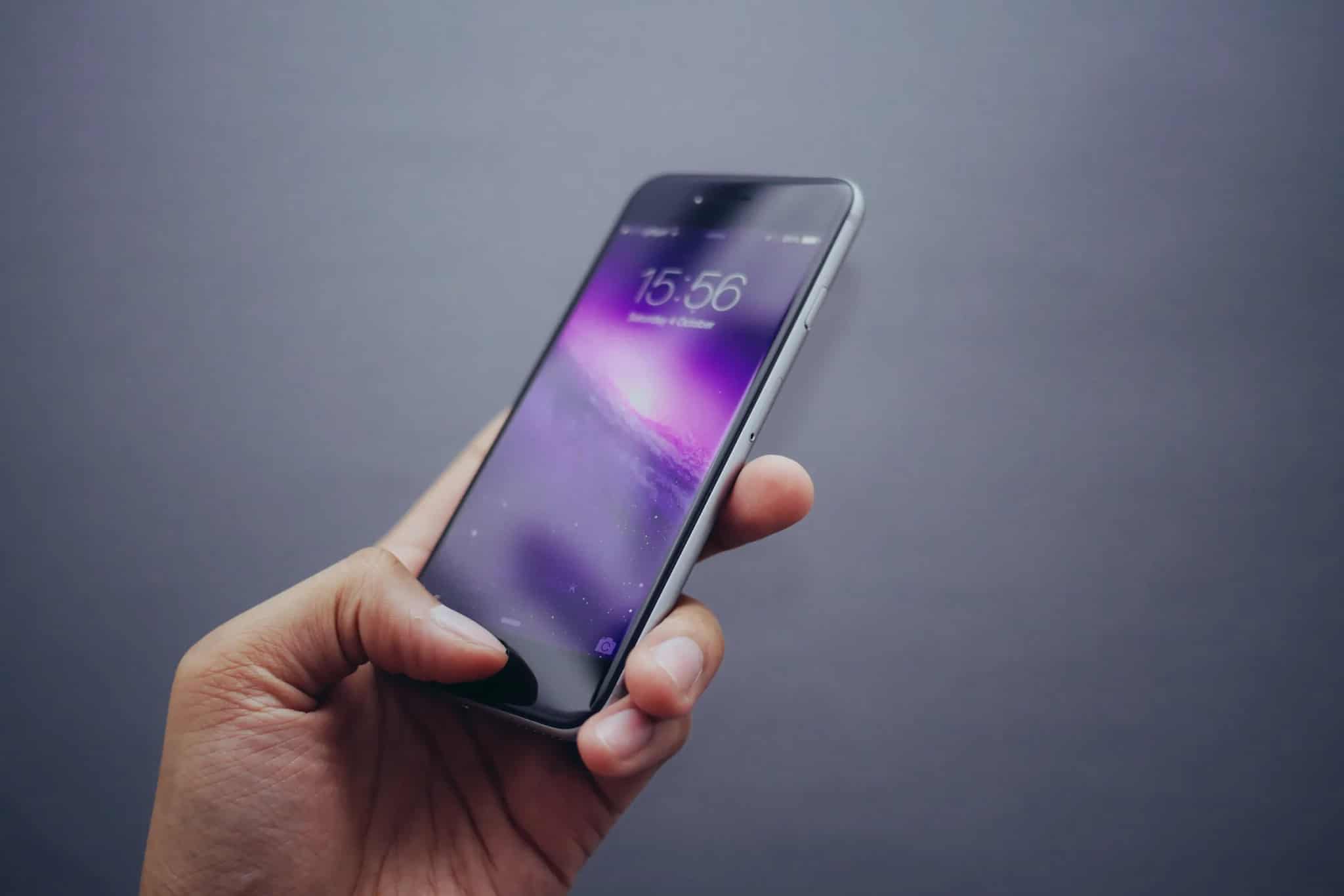A hand holding a smartphone displaying a lock screen with the time and date.