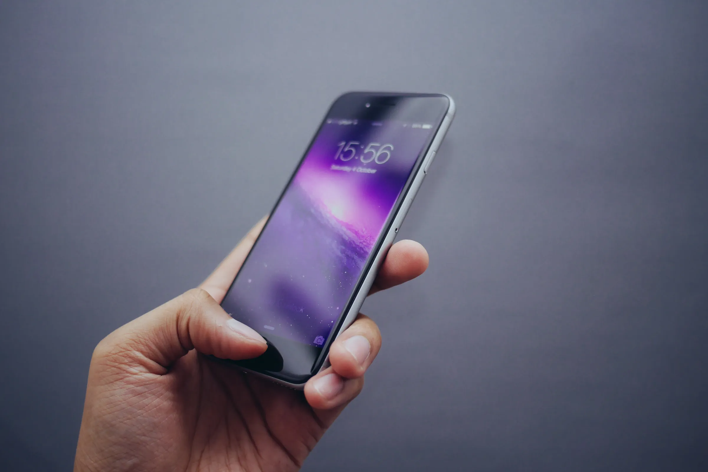 A hand holding a smartphone displaying a lock screen with the time and date.