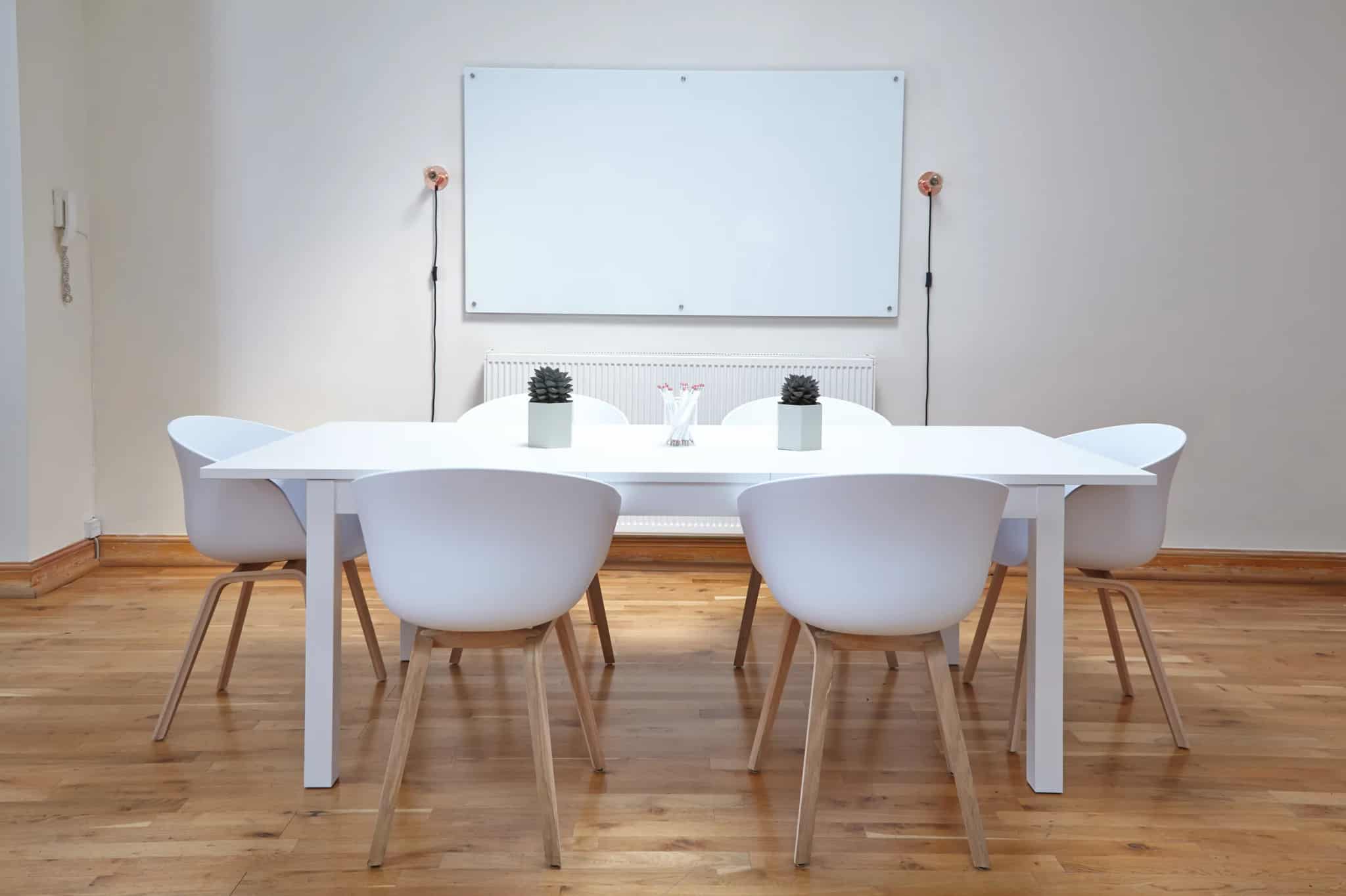 A bright, modern conference room with a white table, chairs, and a whiteboard on the wall.