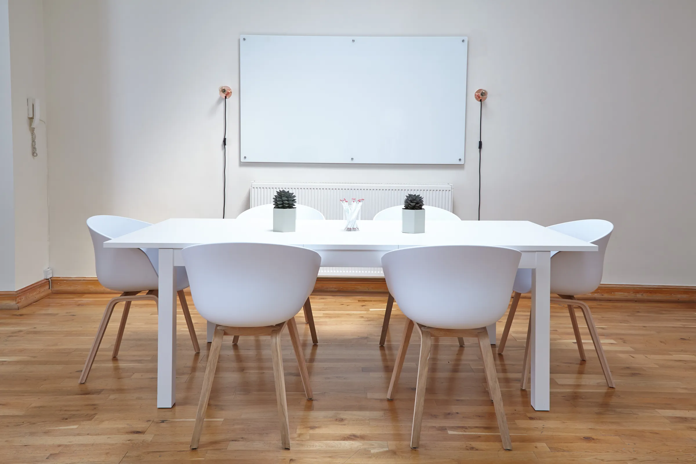 A bright, modern conference room with a white table, chairs, and a whiteboard on the wall.
