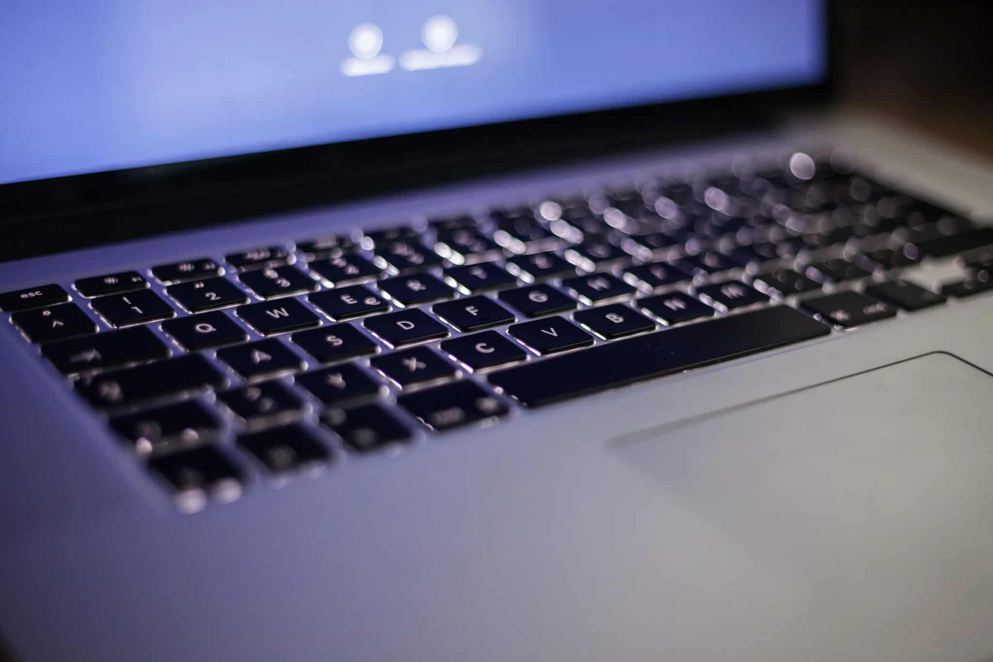 Close-up of a blue backlit laptop keyboard with a softly glowing screen above it.