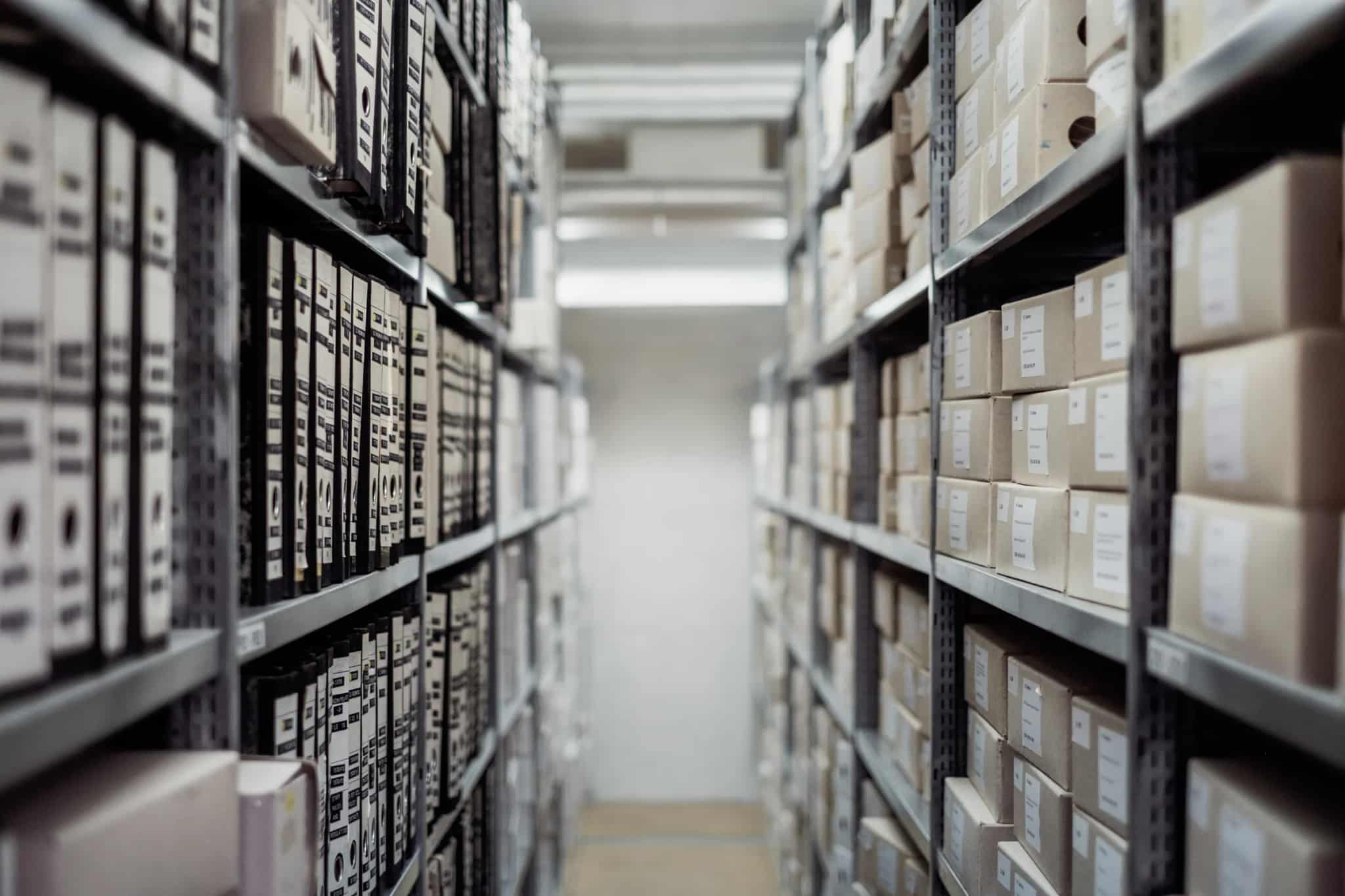 A narrow aisle between metal shelving units filled with labeled archive boxes and binders.