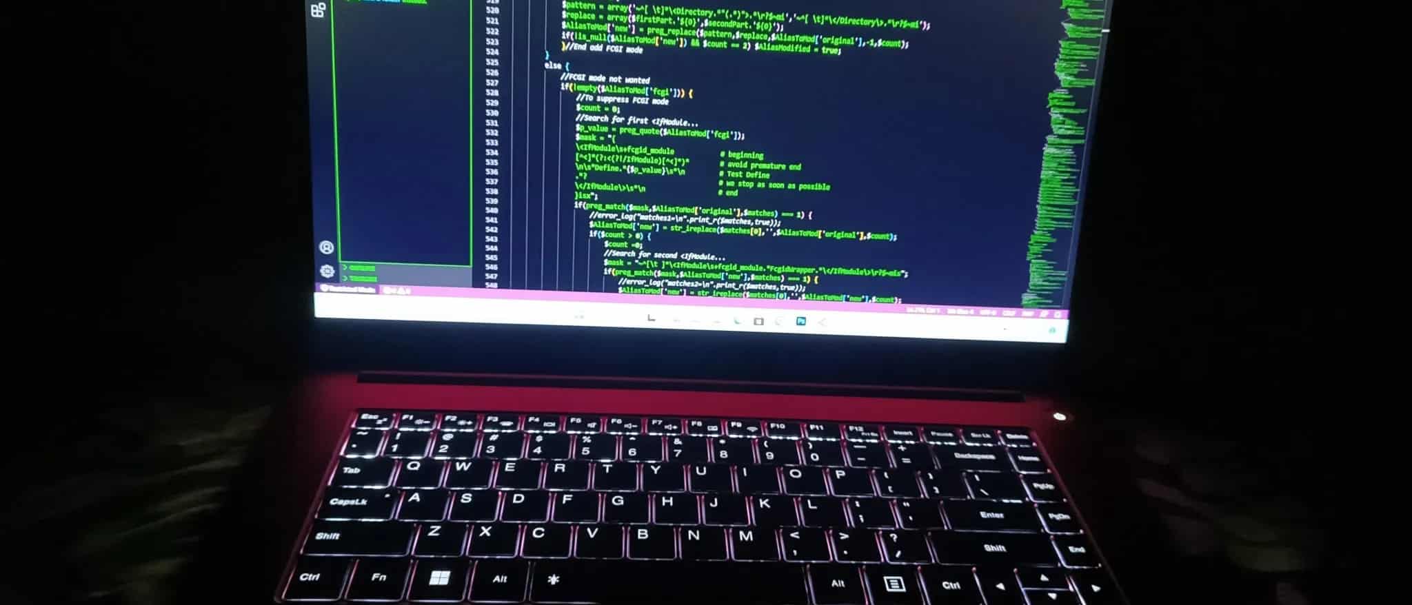 A laptop screen glows with green programming text in a darkened room.