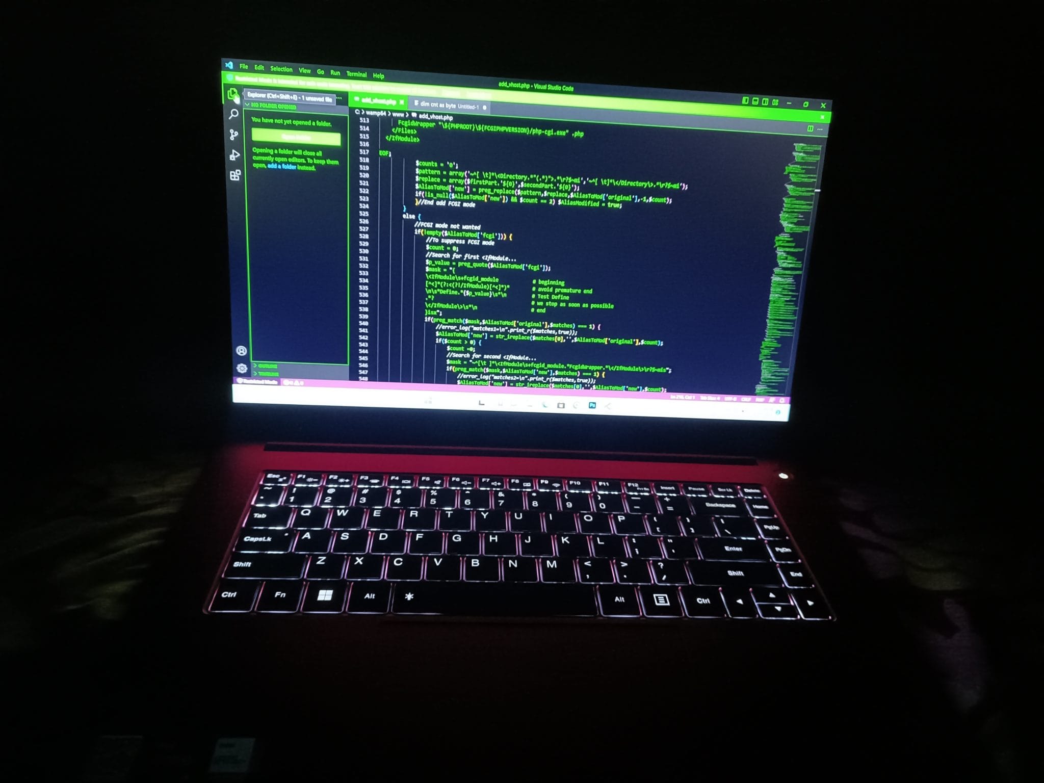 A laptop screen glows with green programming text in a darkened room.