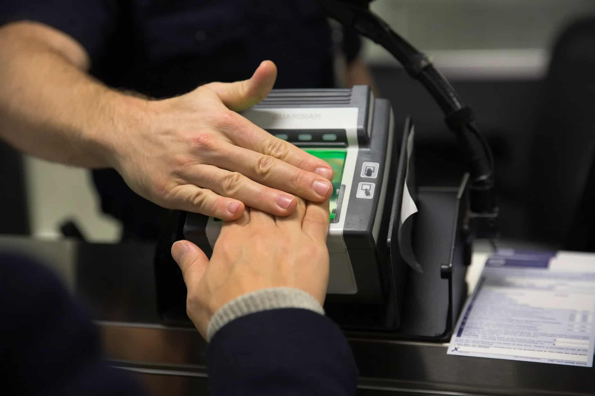 Close-up of two hands placed on a biometric fingerprint scanning device at a checkpoint.