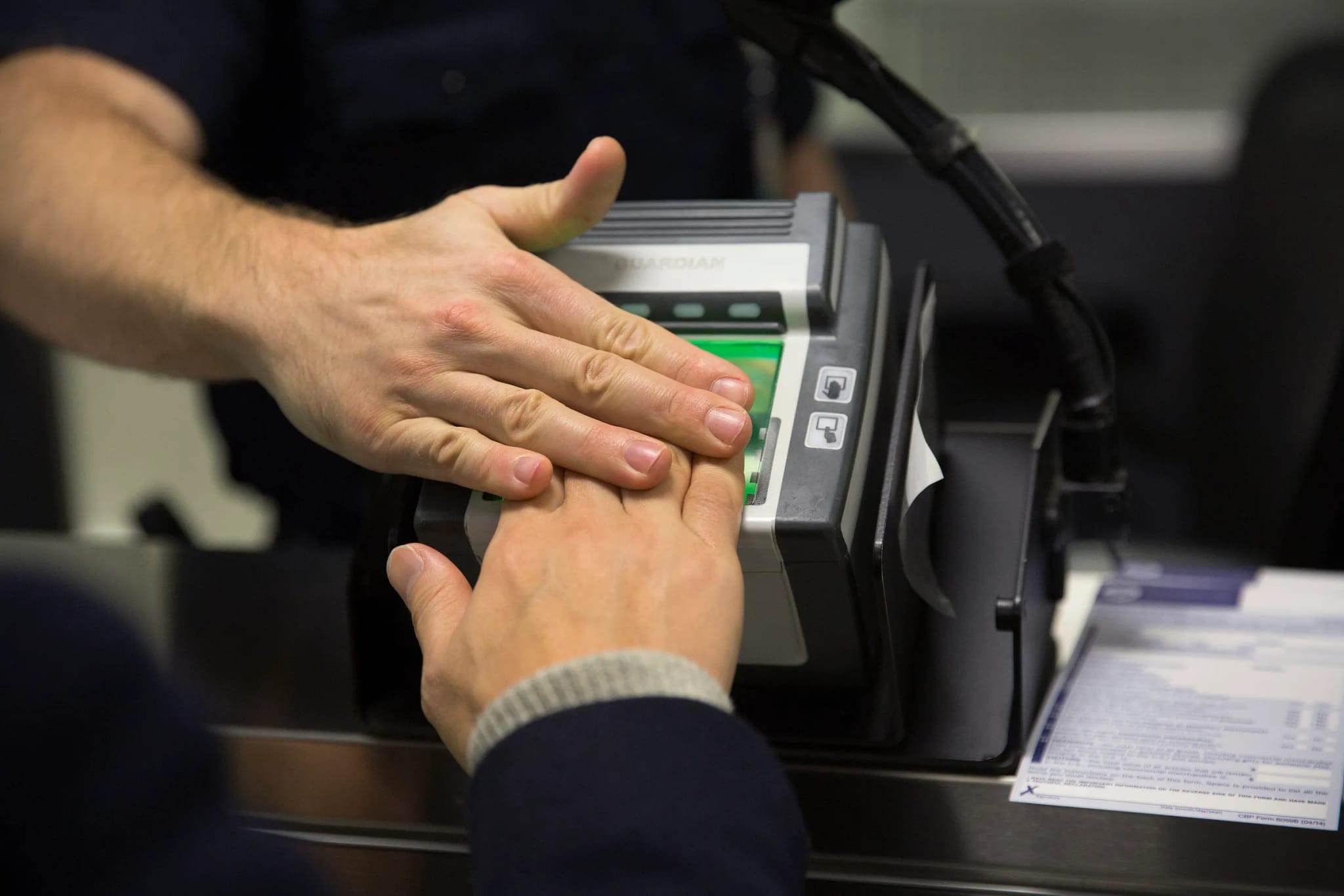 Close-up of two hands placed on a biometric fingerprint scanning device at a checkpoint.