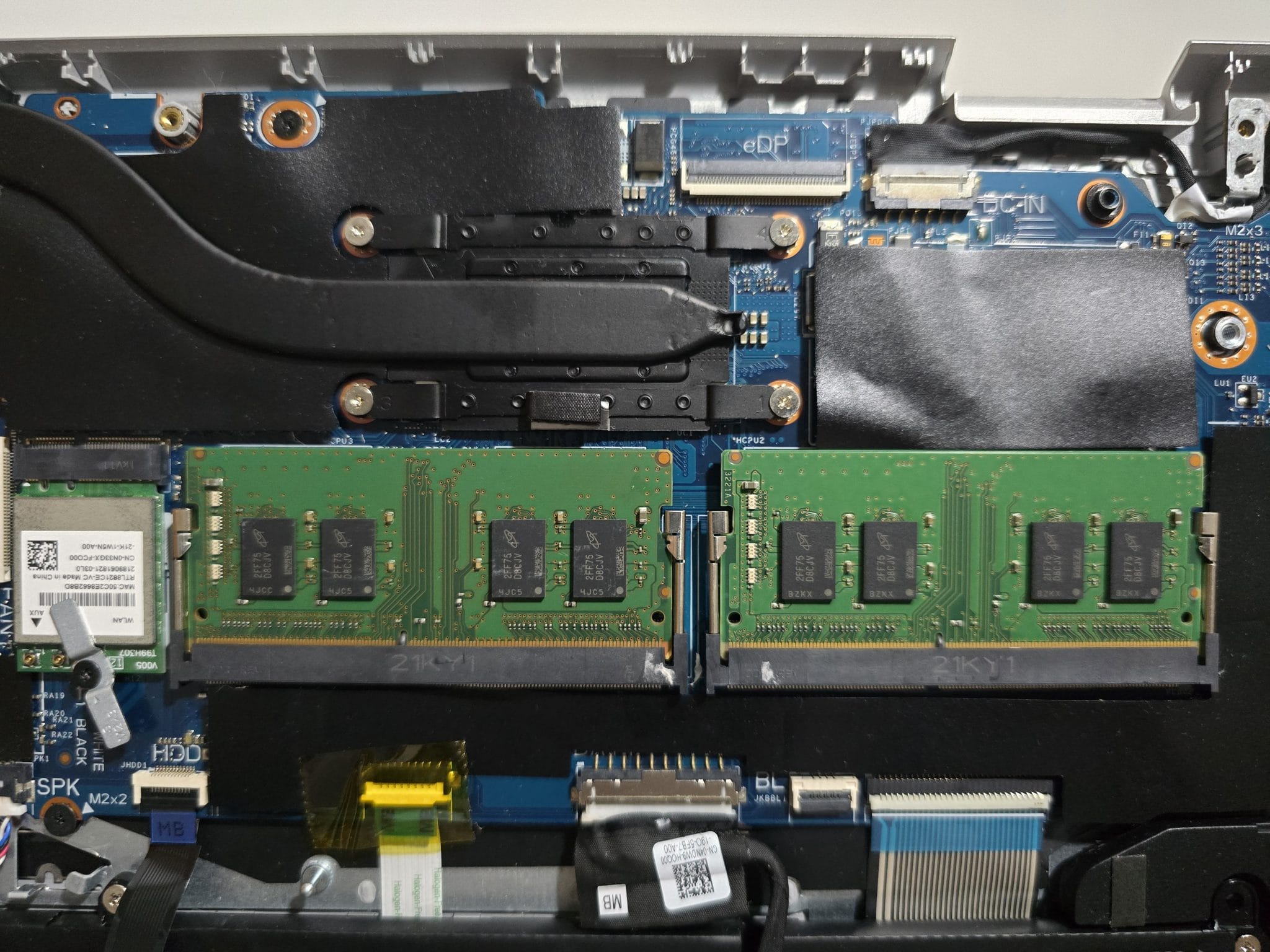 Two green RAM memory modules installed inside an open laptop's motherboard.