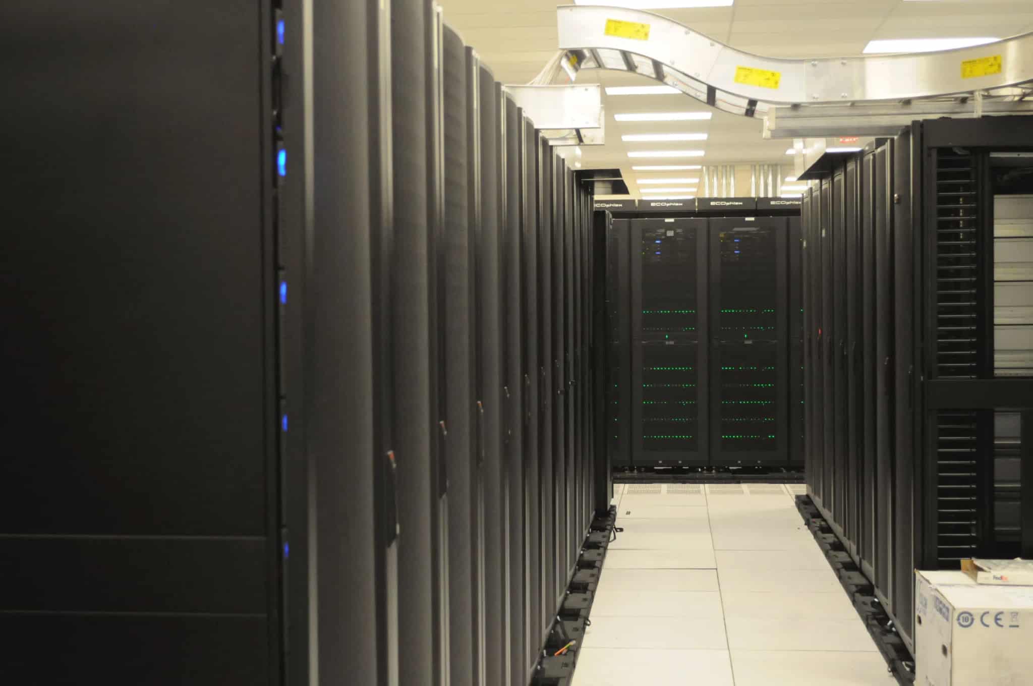 Rows of dark server racks with blinking status lights lining an aisle in a data center.