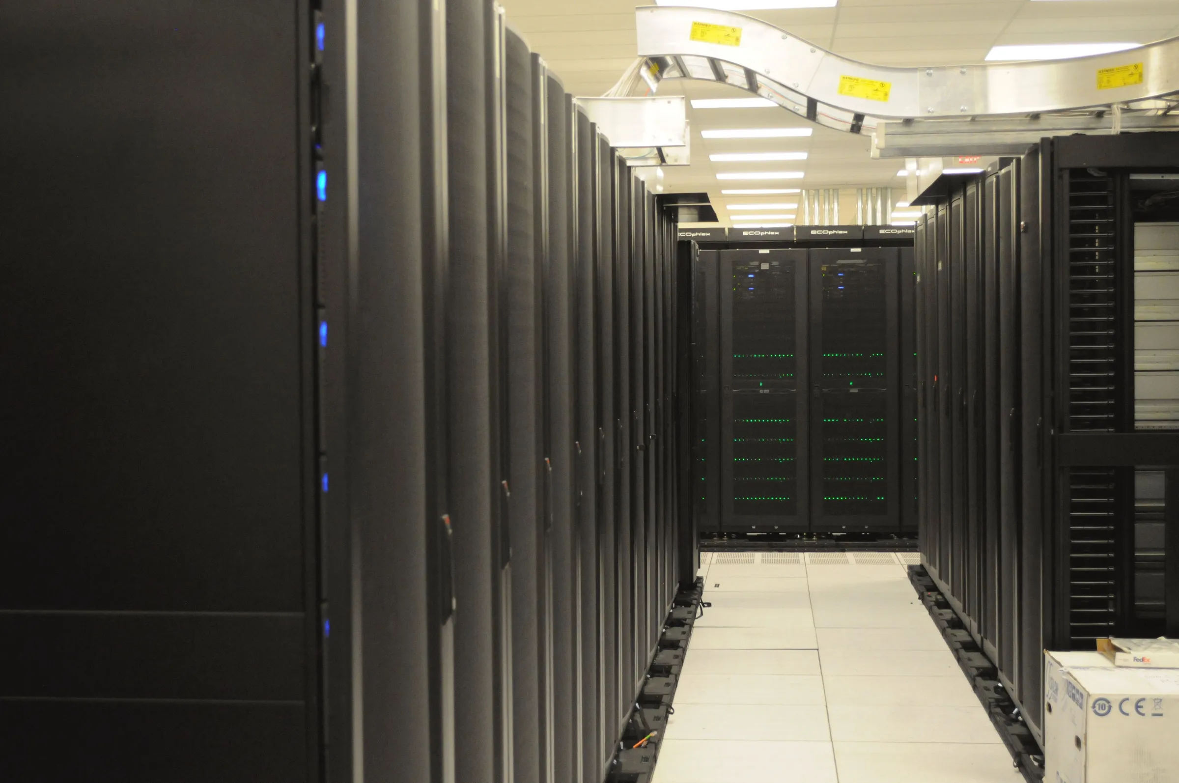 Rows of dark server racks with blinking status lights lining an aisle in a data center.