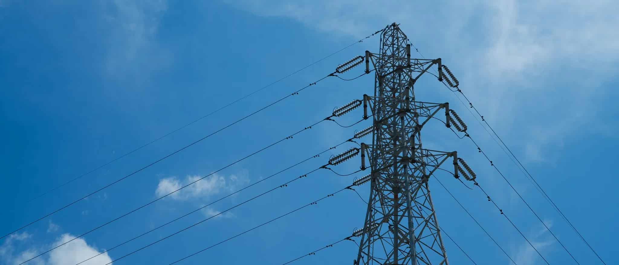 An electrical transmission tower carrying power lines against a clear blue sky.