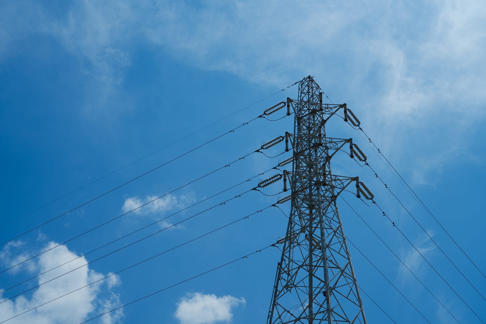An electrical transmission tower carrying power lines against a clear blue sky.