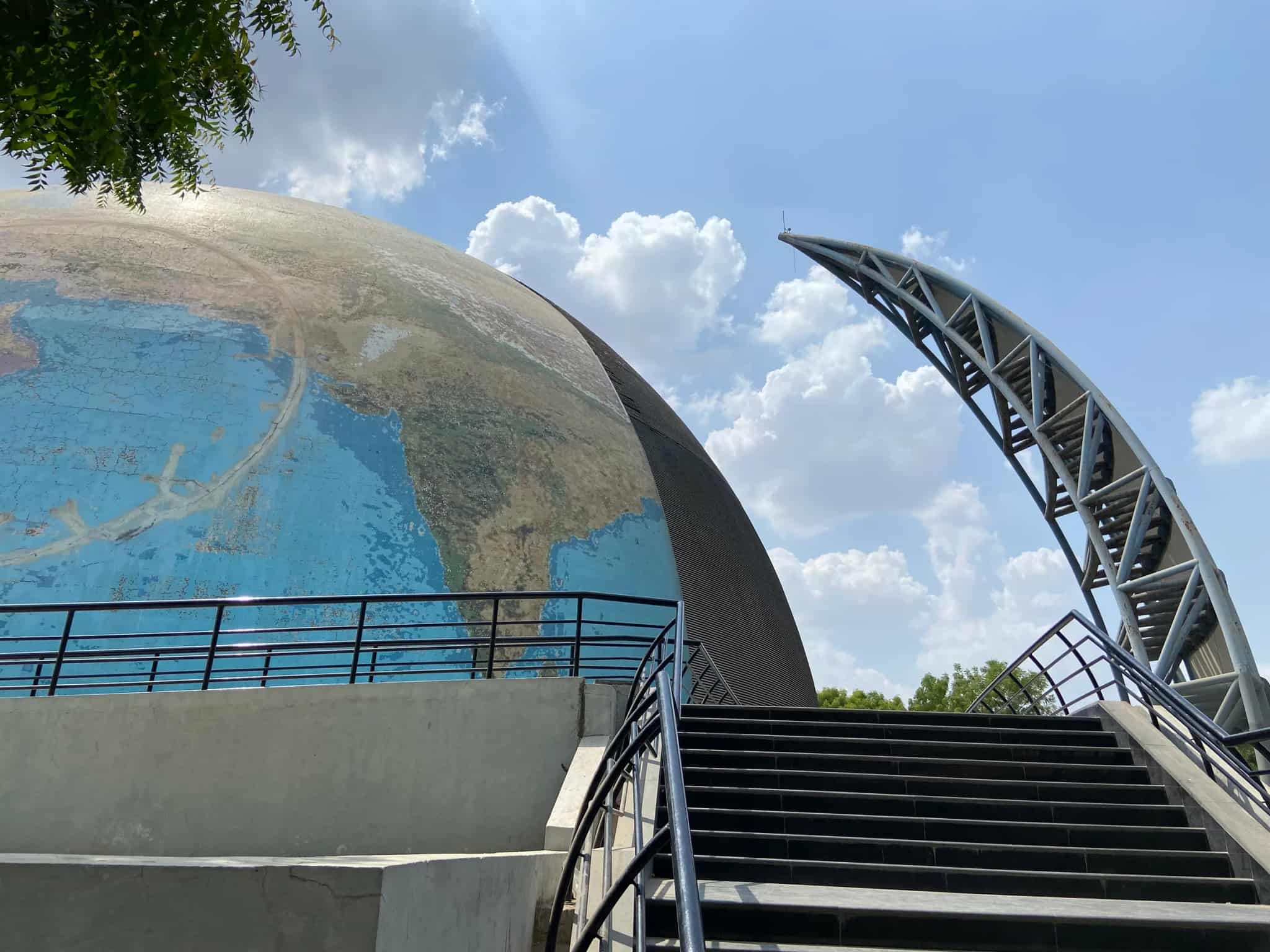 A large spherical globe monument showing a world map, photographed from below against a blue sky with clouds.