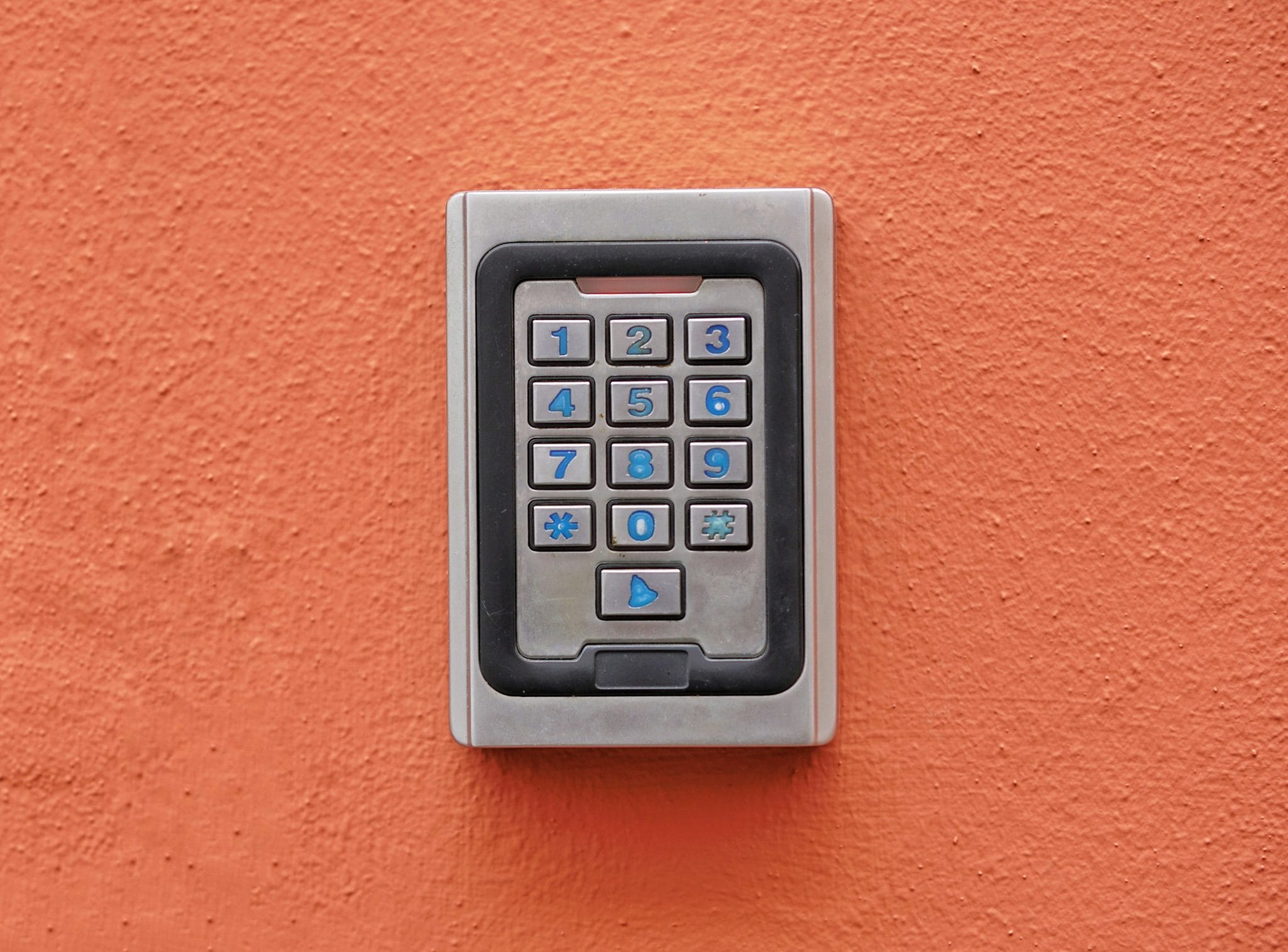 A numeric keypad access control device mounted on an orange wall.