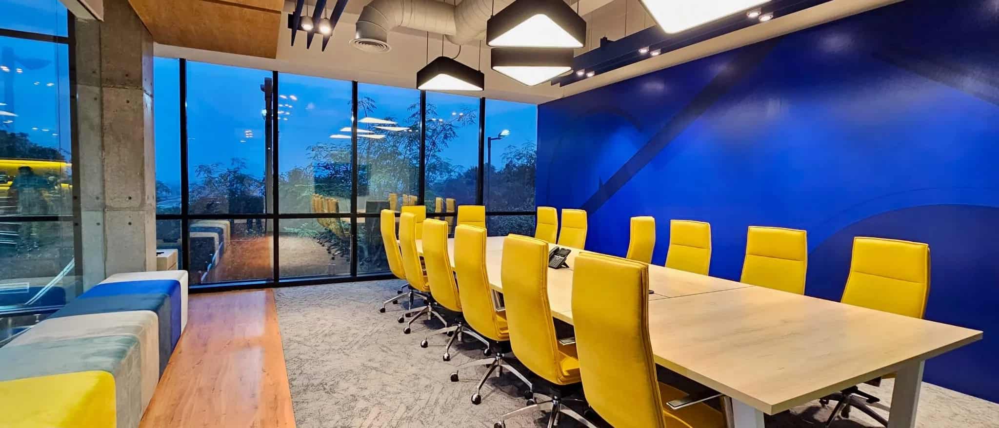 An empty modern conference room with a long wooden table and vibrant yellow chairs.