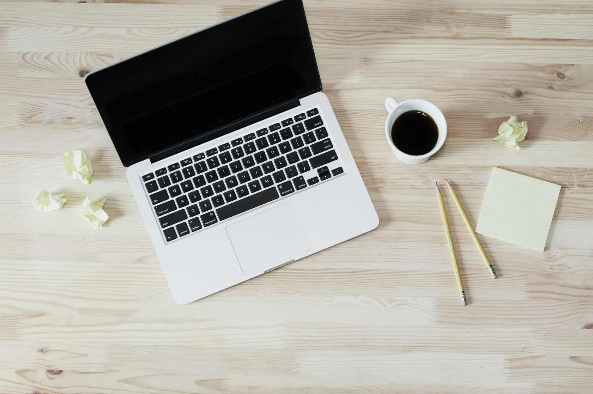 An overhead view of an open laptop, a cup of coffee, and pencils on a wooden desk.